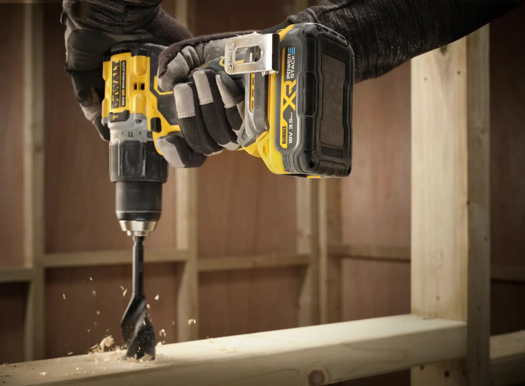 Close-up of a DEWALT drill with DCBP318 battery in use, drilling into wood at a construction site.