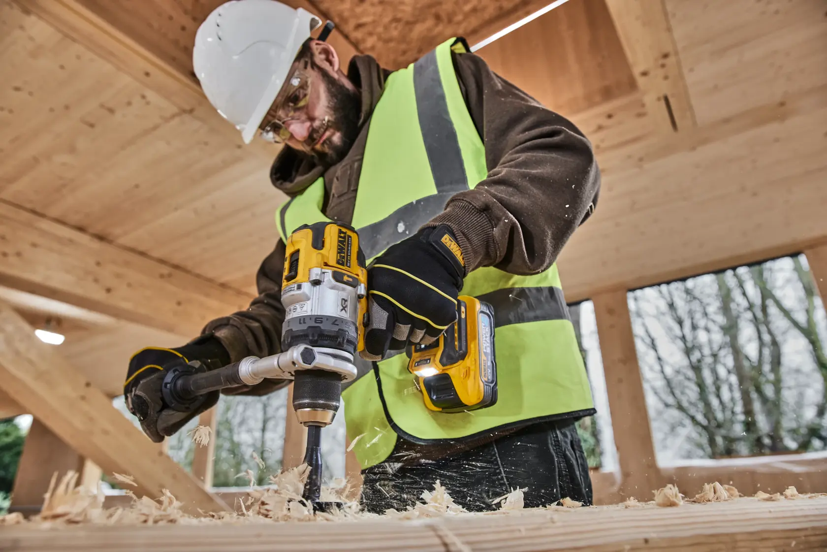 Trabajador usa DEWALT DCD1007NT y DCZ607X2-XE en madera. Categoría fotografía. Usa equipo de seguridad.