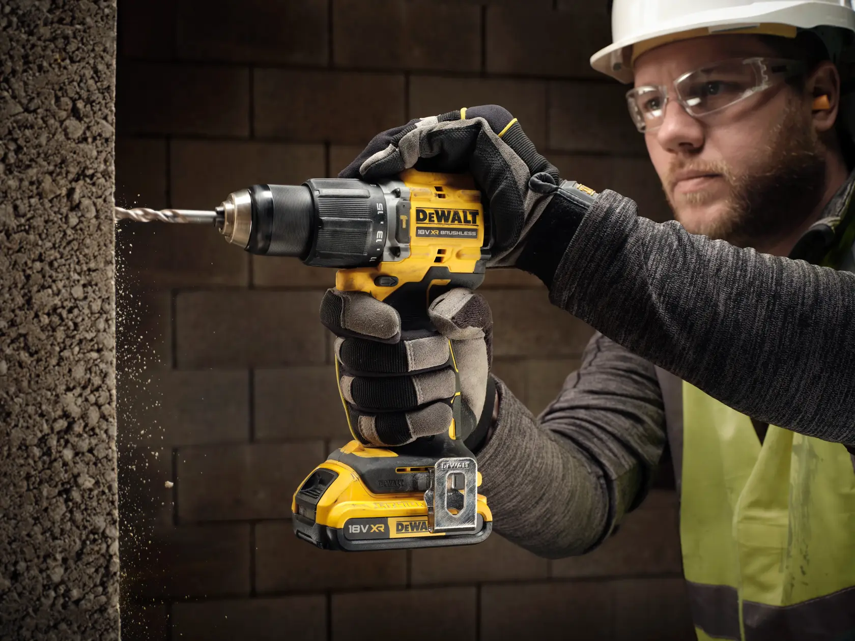 Gloved hand drills concrete with a DEWALT DCD799D2T cordless tool. Construction setting, close-up action.