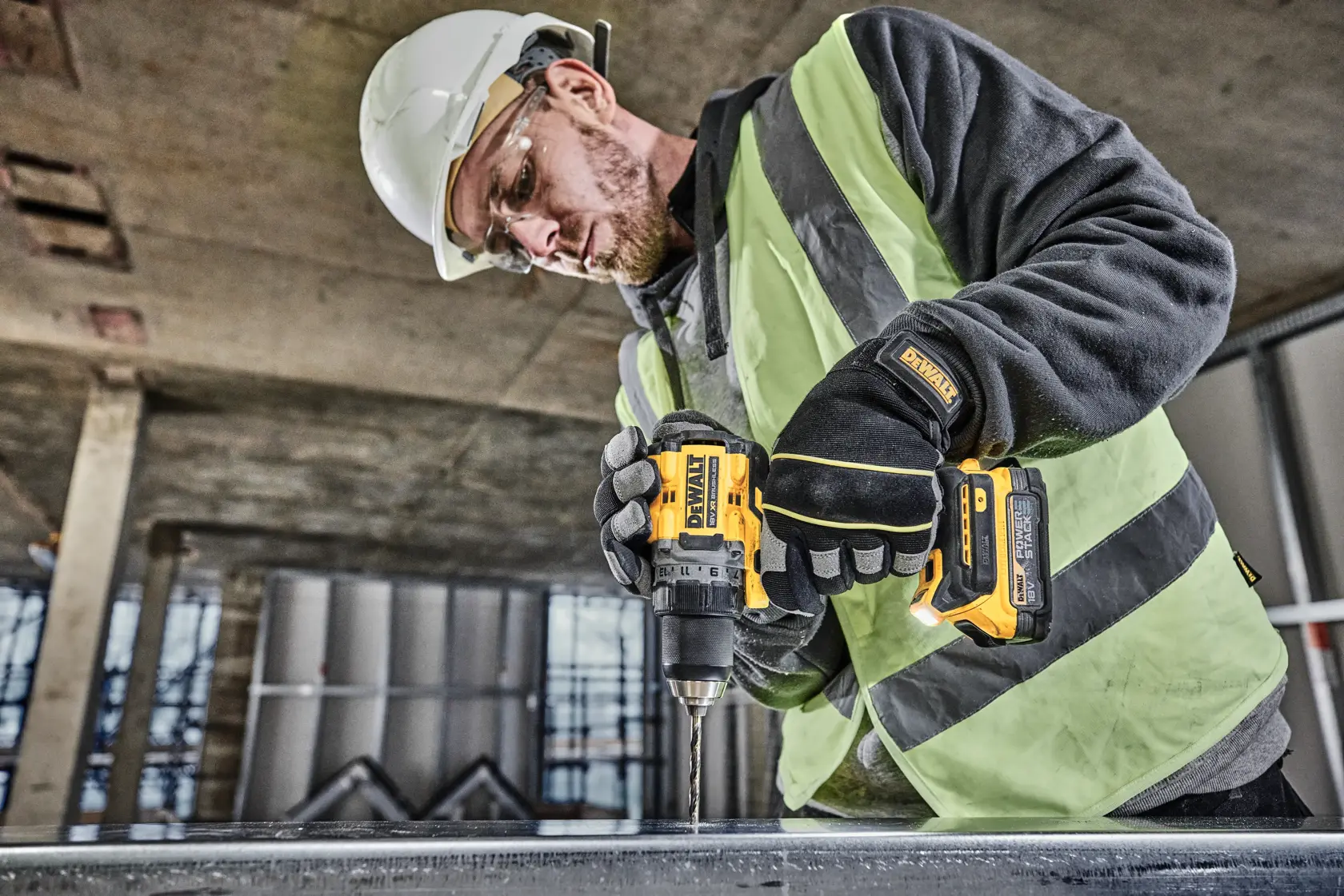 A person wearing a safety helmet, gloves, and a high-visibility vest is using a DEWALT DCD800E1T cordless drill to drill