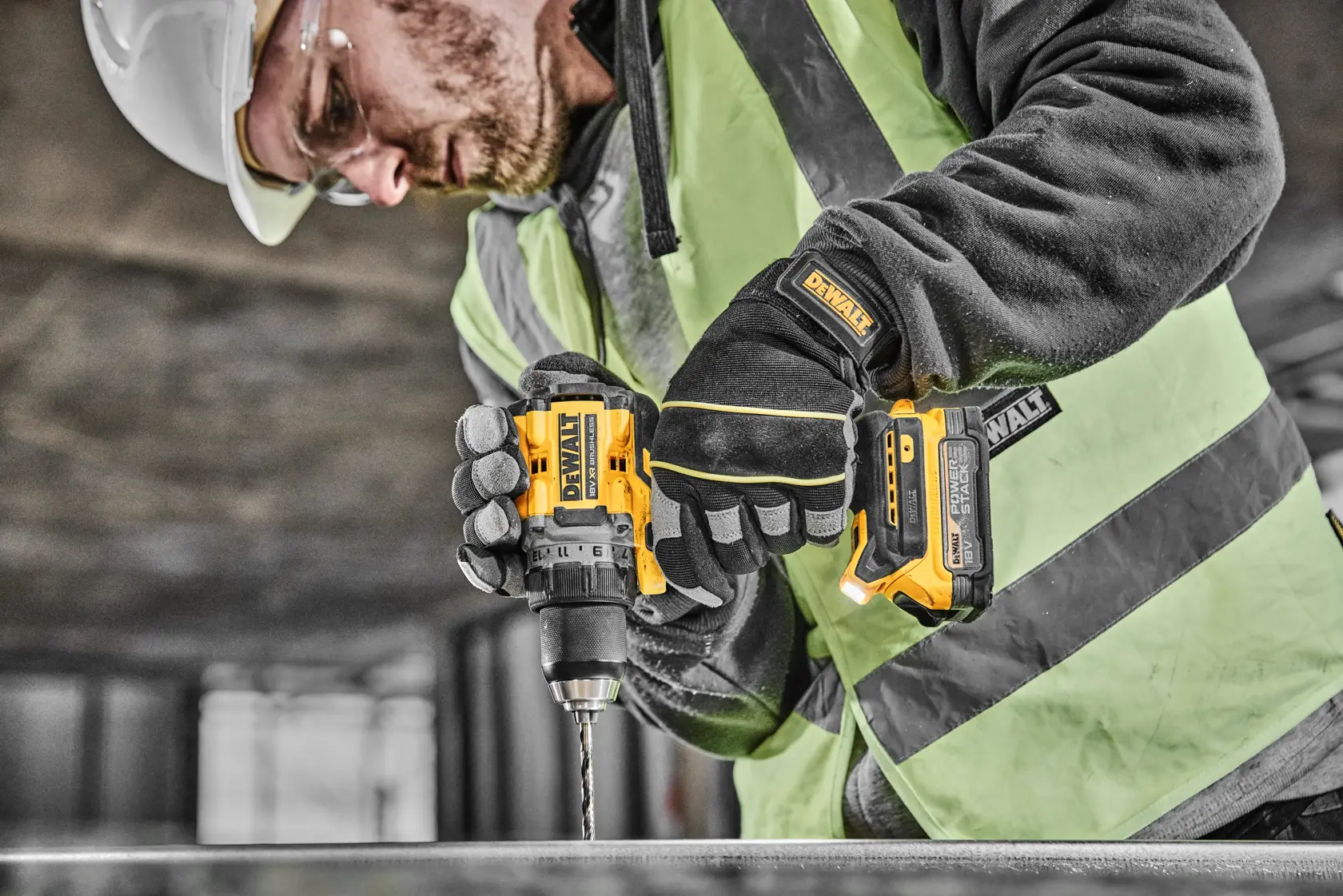 Un trabajador de la construcción con equipo de seguridad utiliza un taladro inalámbrico DEWALT (modelo DCD800E2T) para perforar una superficie metálica en un entorno industrial.