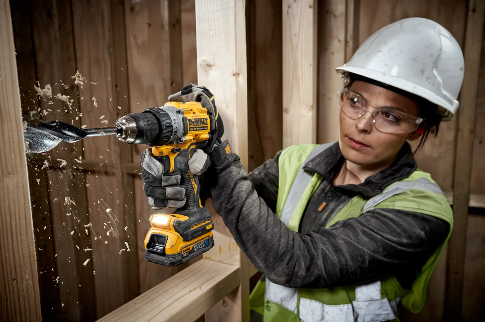 Persona perfora madera con un taladro DEWALT inalámbrico y equipo de seguridad en obra.