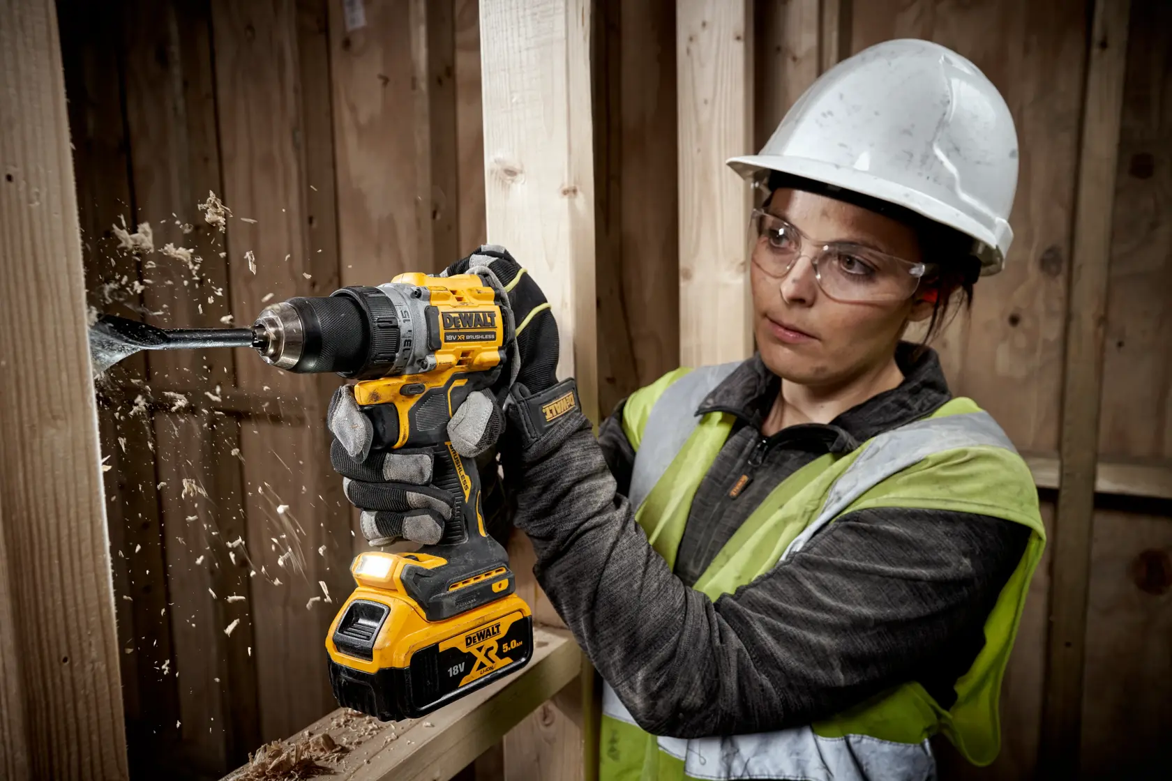 Personne perce du bois avec une DEWALT DCD800P2T, portant un casque et des gants sur chantier.