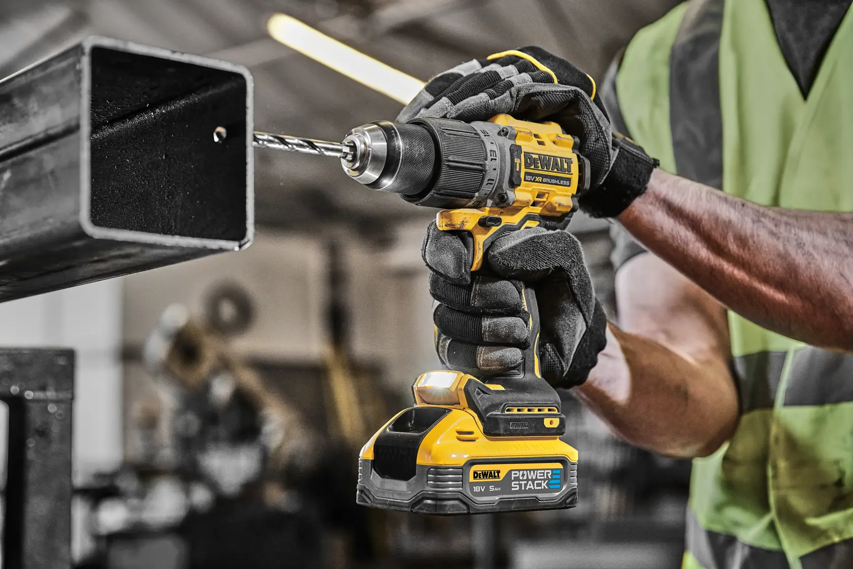 Trabajador con guantes perfora metal con taladro inalámbrico amarillo DEWALT en taller industrial.