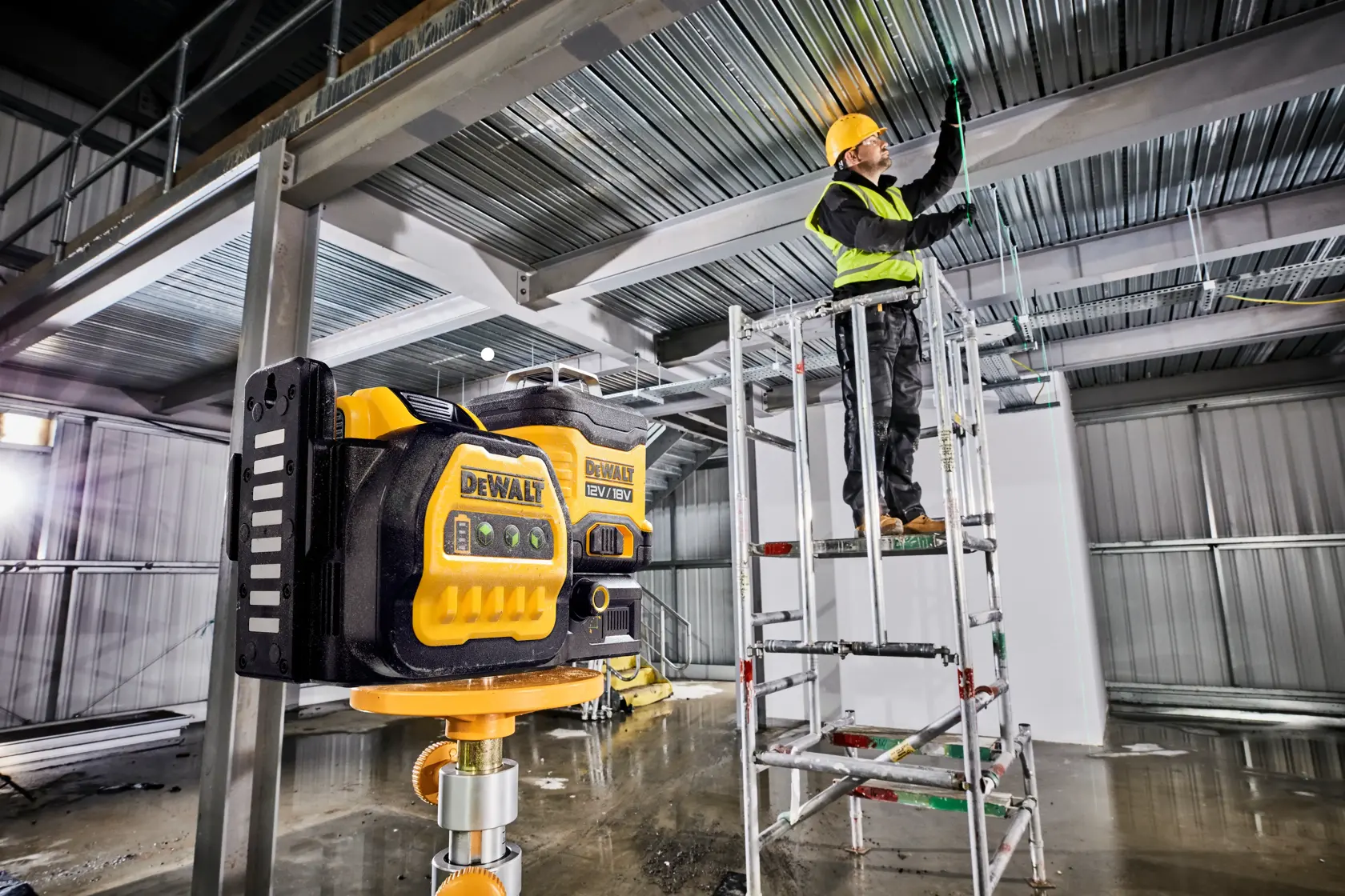 DEWALT laser level used at a construction site, worker adjusts ceiling wiring on a scaffold.