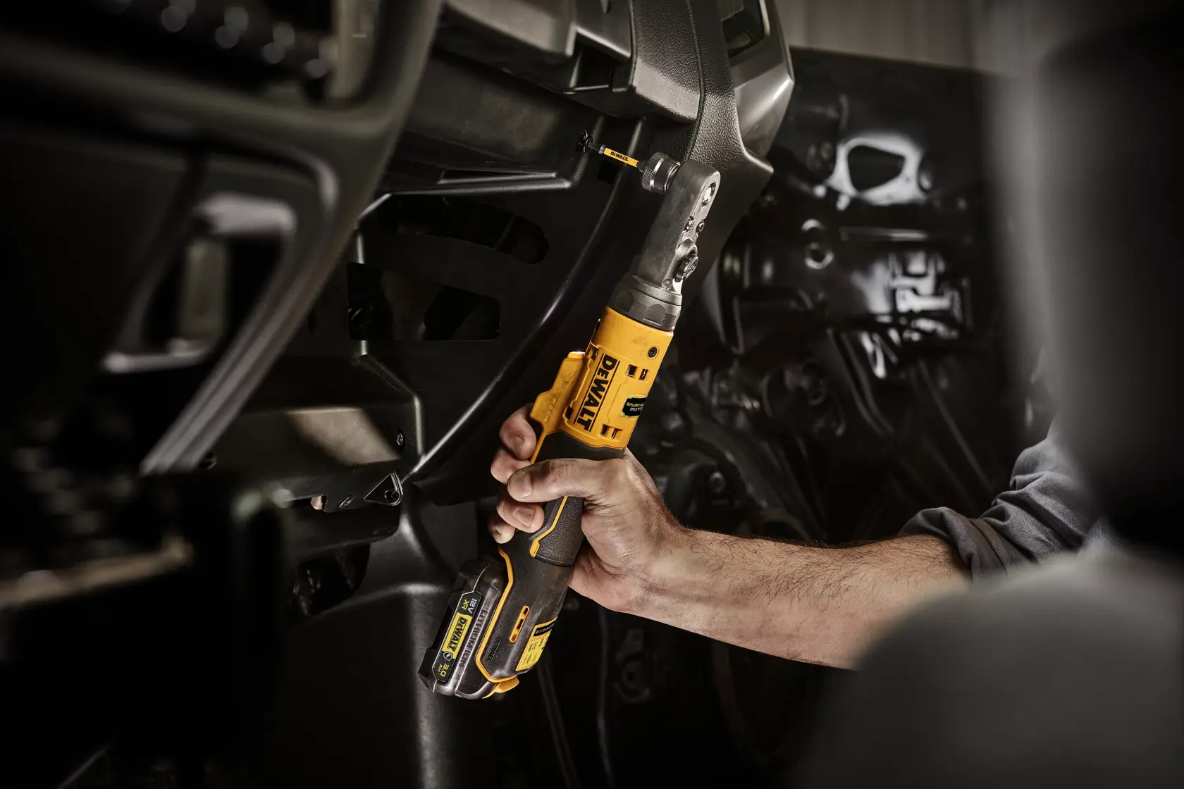 Mano usa llave de carraca inalámbrica DEWALT en el área del tablero de un vehículo.