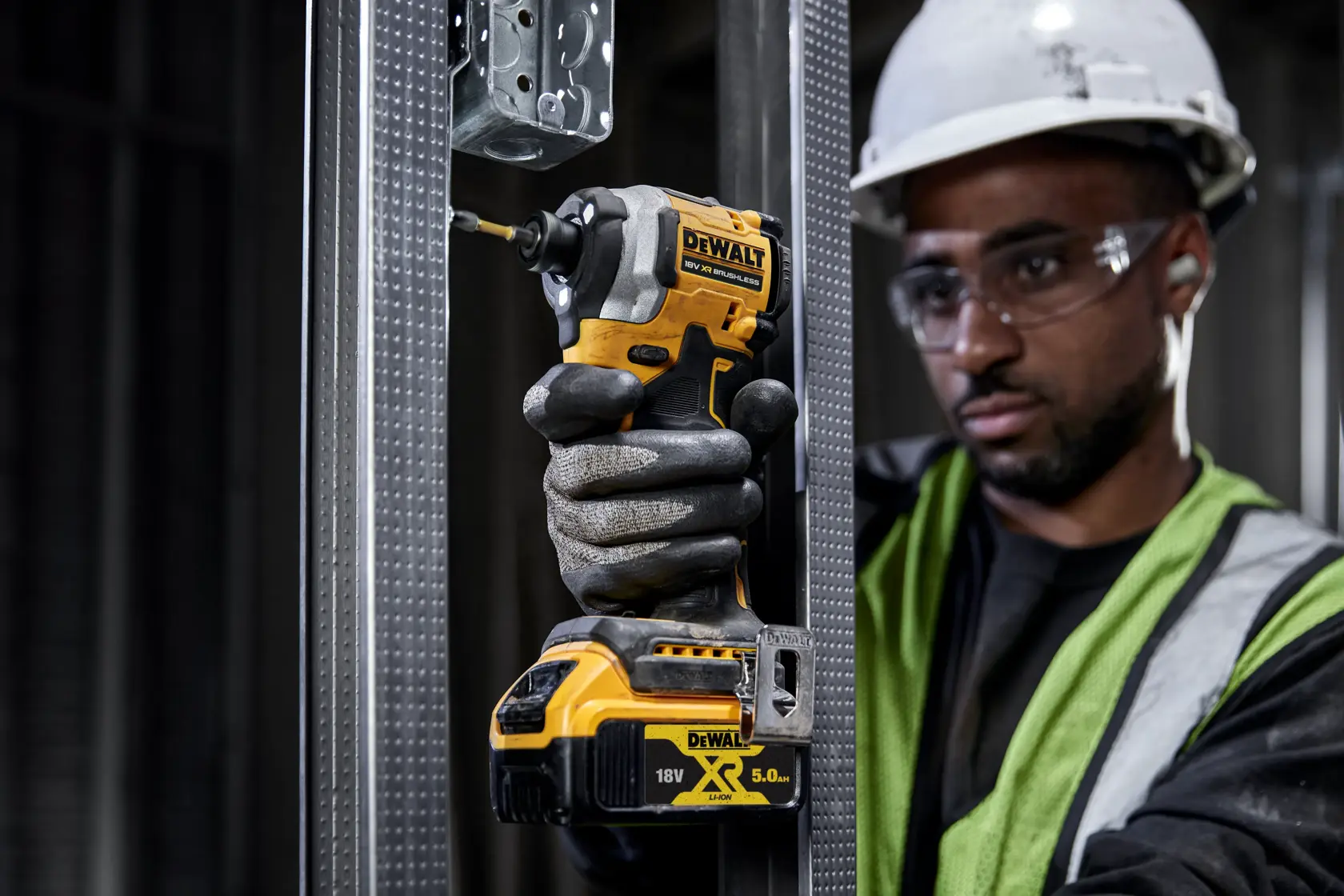 Trabajador usa atornillador DEWALT DCF850P2T a batería sobre estructura metálica en obra.