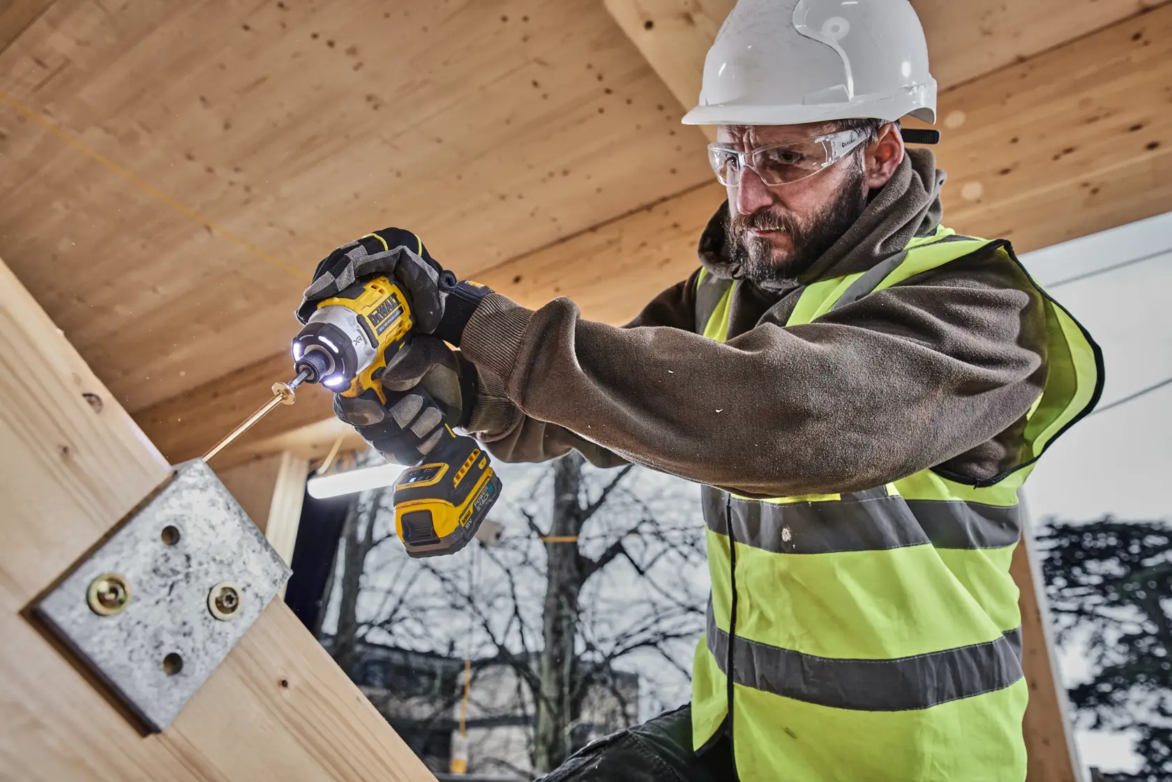 DEWALT DCK2201P1T1-XE y DCF860NT usados por trabajador perforando placa metálica en obra.
