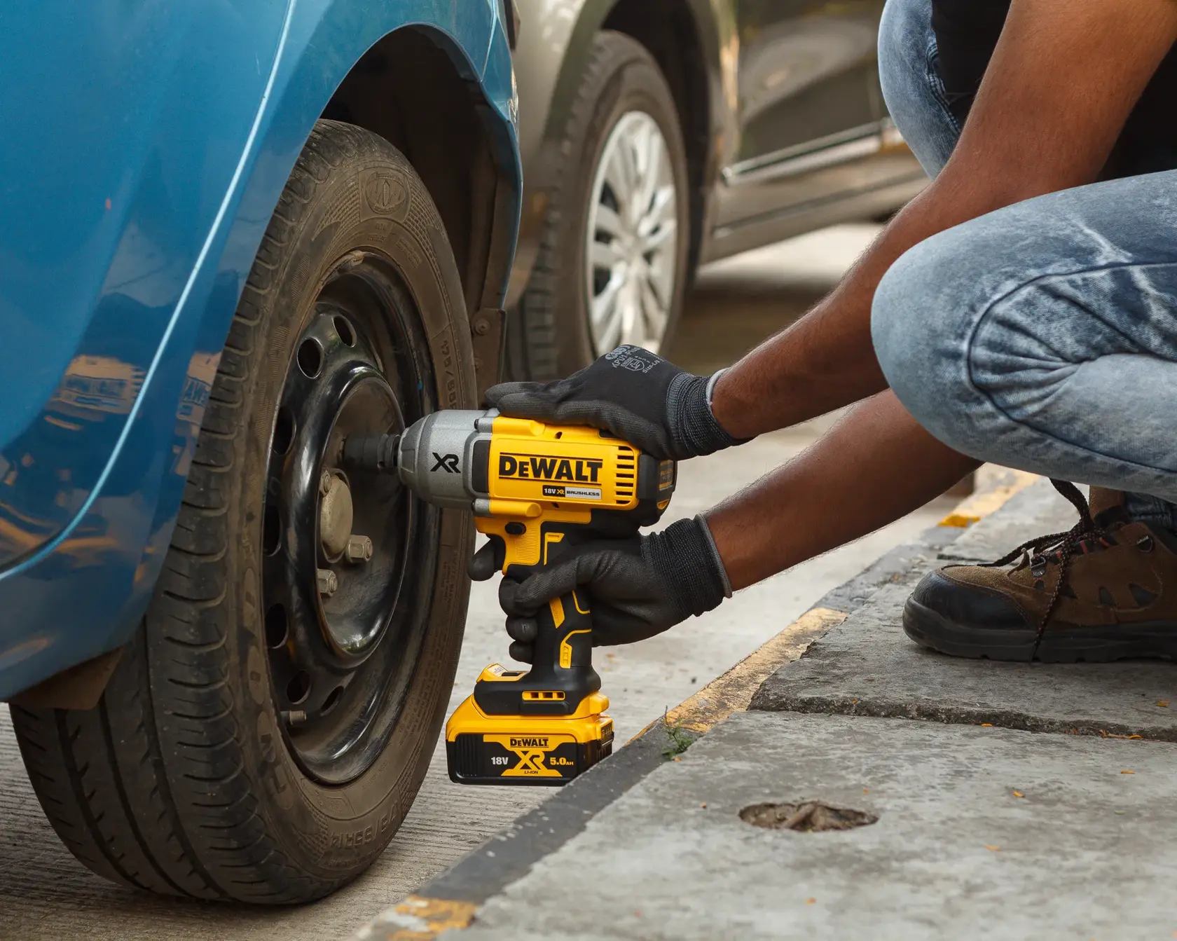 Person uses DEWALT cordless impact wrench to tighten car wheel bolts outdoors.