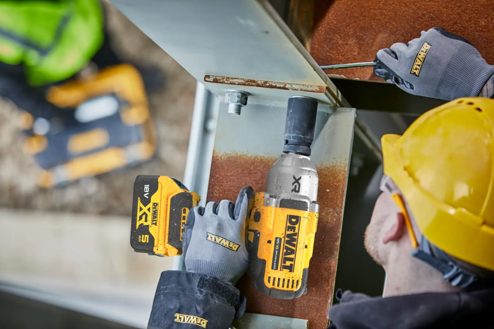 Trabajador usa llave de impacto DEWALT sin cable en viga metálica, con guantes y casco amarillo.