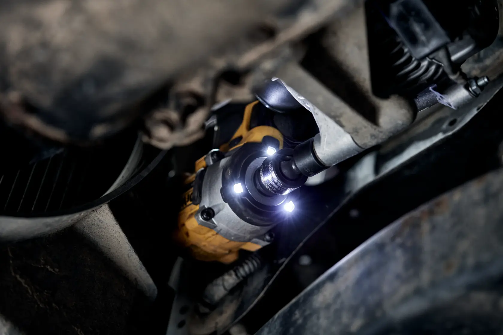 Nahaufnahme eines DEWALT Akku-Schlagschraubers, der am Unterboden eines Fahrzeugs verwendet wird, mit integrierten LED-Leuchten, die den Arbeitsbereich ausleuchten.