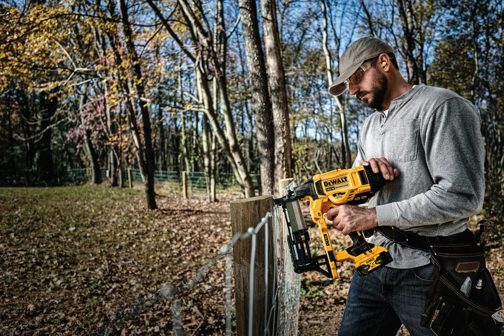 Person using DEWALT cordless fencing nailer to build a wooden fence outdoors in a forested area.