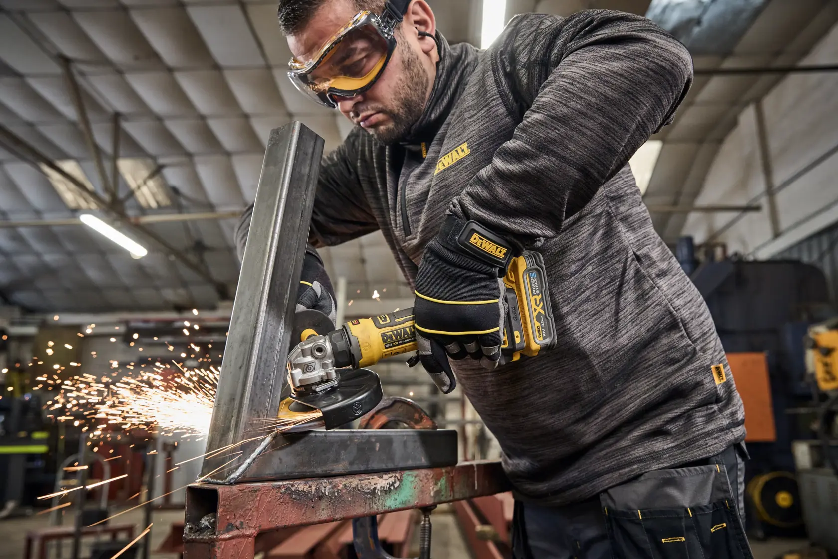 DEWALT angle grinder cutting metal with sparks. Worker wearing gloves in an industrial workshop.
