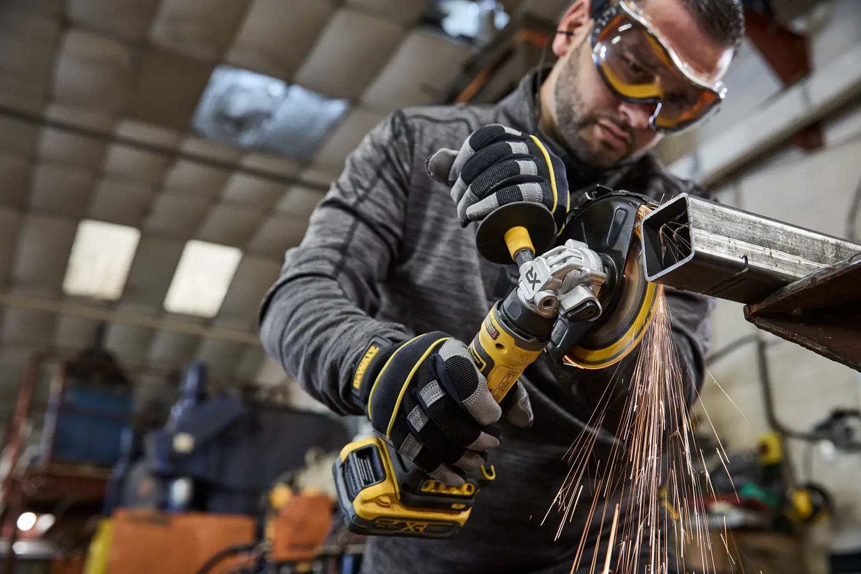 Person using a DEWALT cordless grinder on metal, with sparks flying, in an industrial workshop.