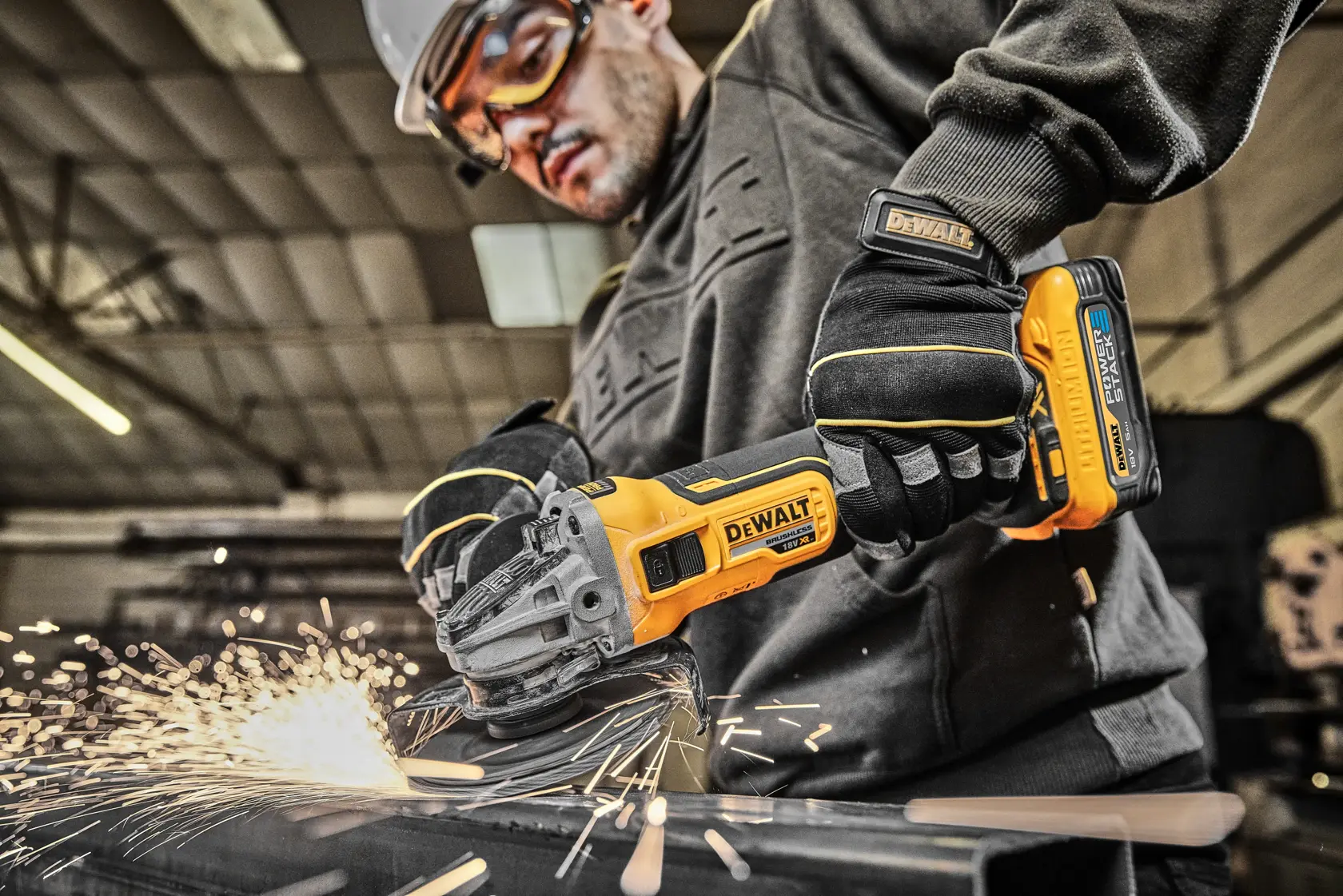 DEWALT cordless grinder in use, cutting metal with sparks, worker wearing gloves and safety gear in workshop.
