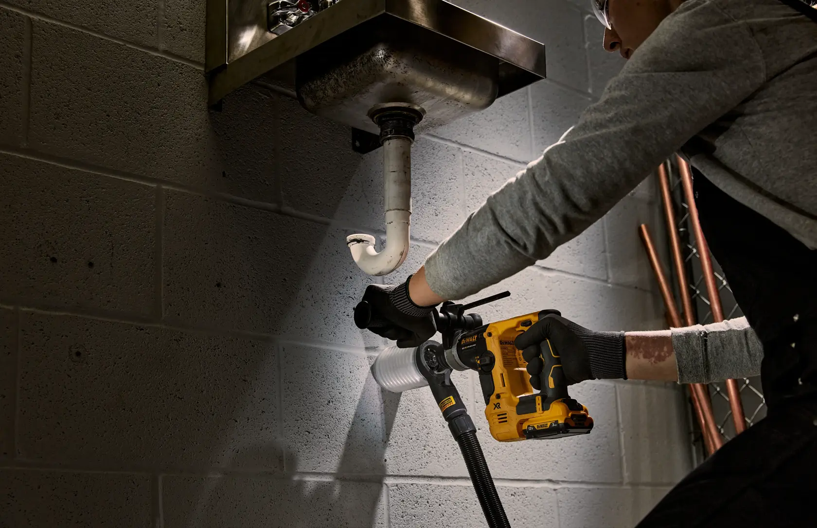 Une personne utilise une perceuse DEWALT sans fil sous un évier pour travailler la plomberie contre un mur.