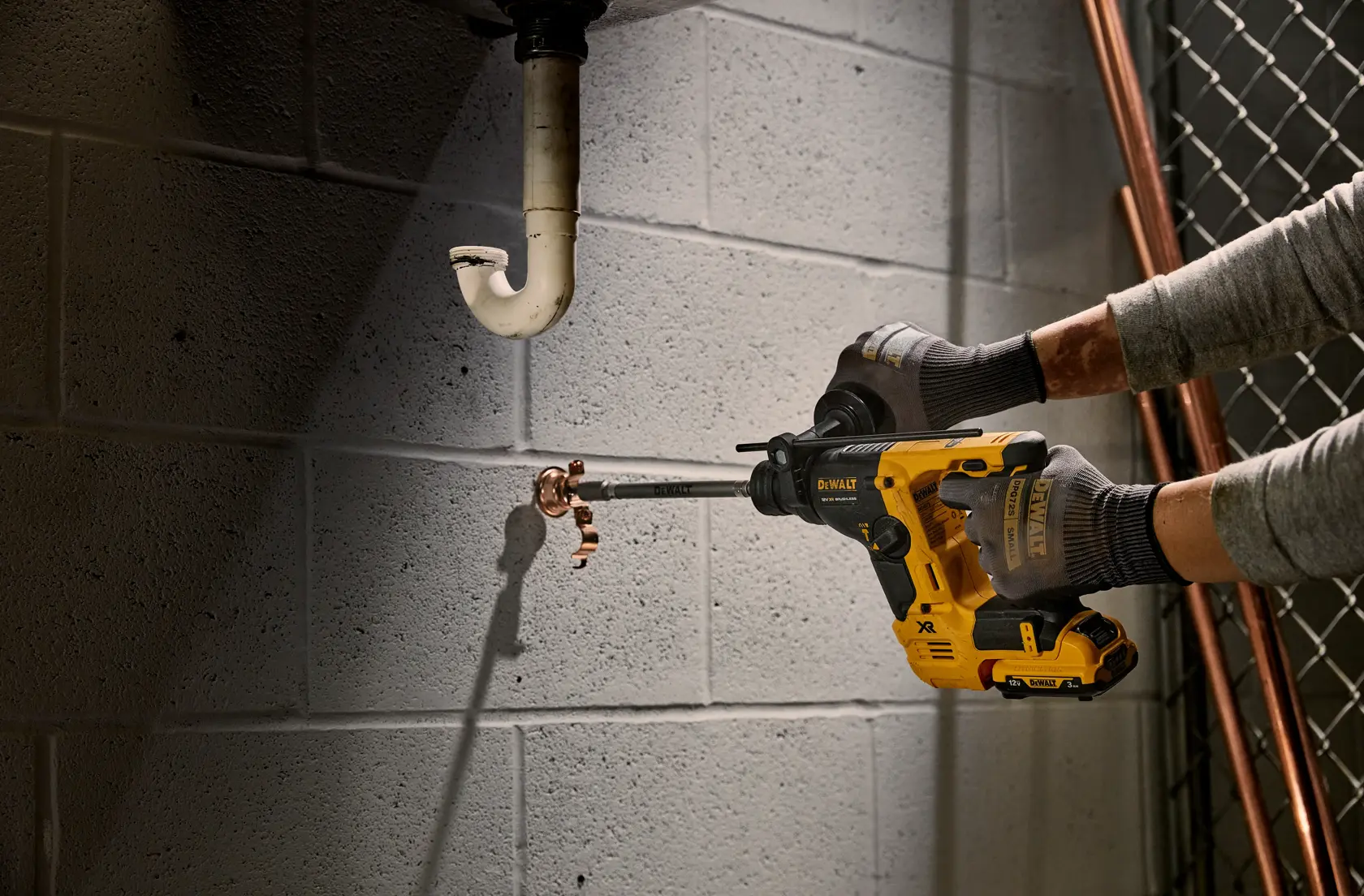 Une personne utilise une perceuse DEWALT pour percer un mur en béton près de tuyaux.