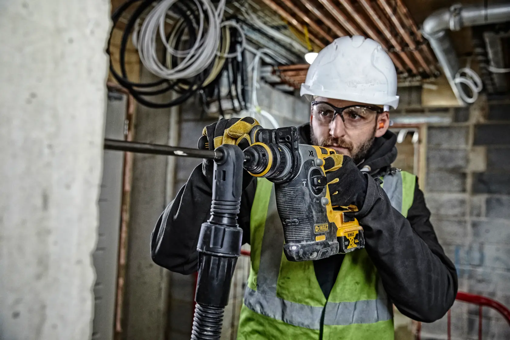 Worker uses a DEWALT rotary hammer drill on a construction site wearing safety gear and a high-visibility vest.