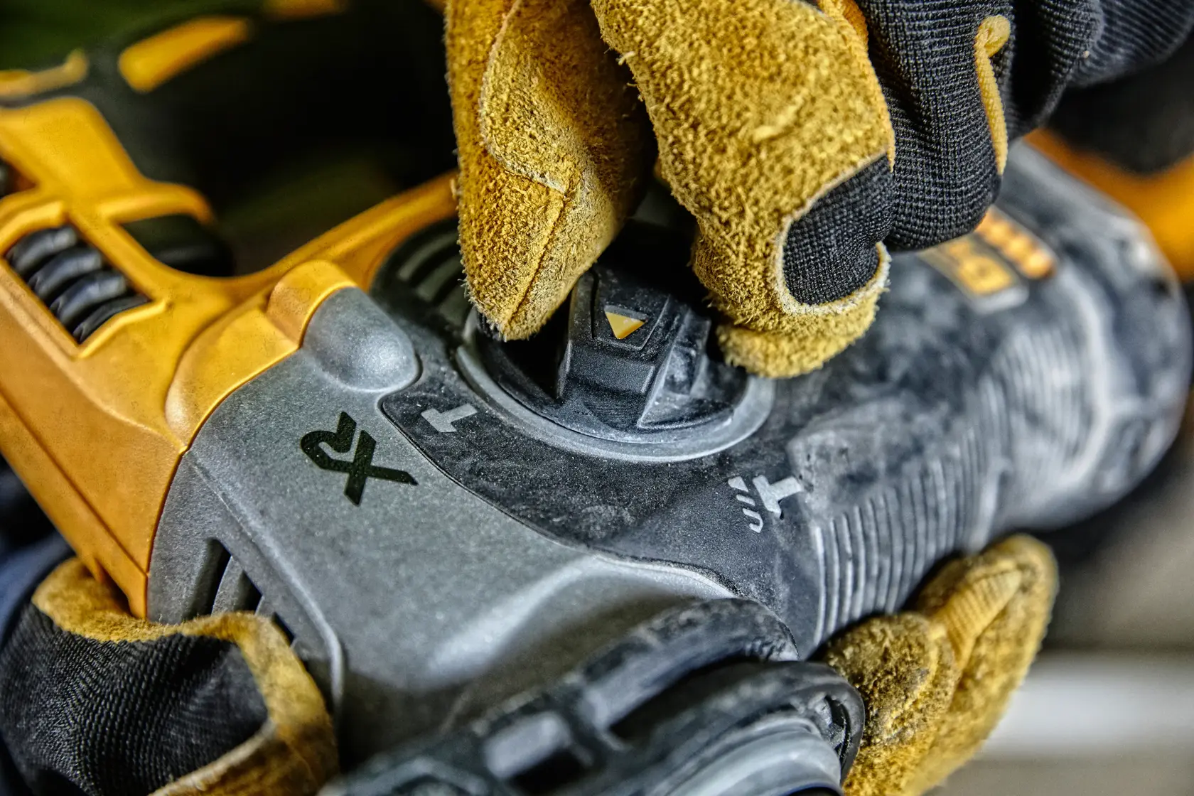 Gloved hand adjusting the mode selector on a DEWALT power tool, close-up view of dial and tool details.