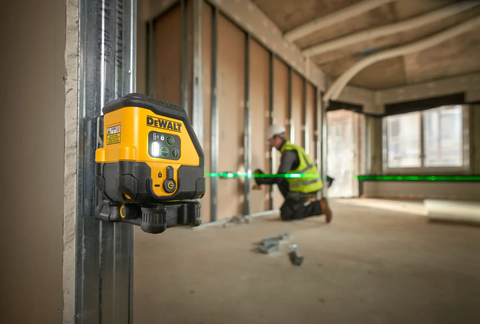 Livella laser DEWALT proietta linea verde. Operaio installa pannelli a muro in cantiere.