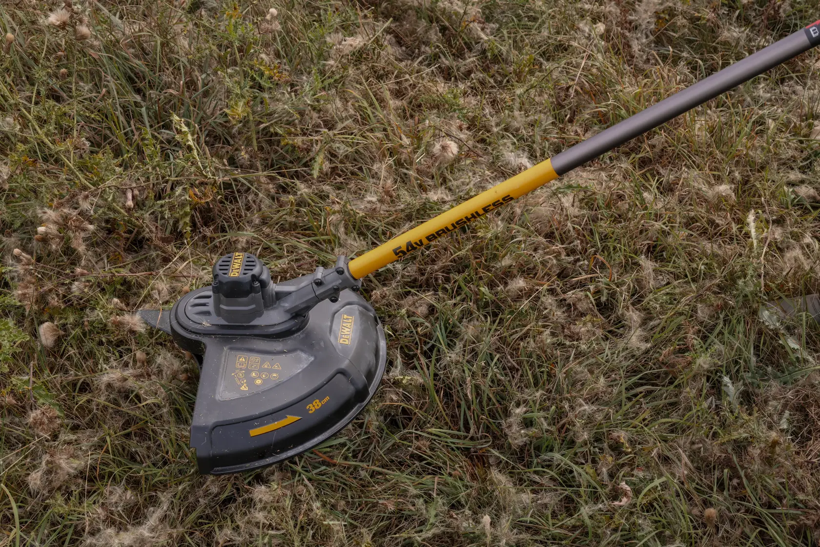 Desmalezadora DEWALT inalámbrica con eje amarillo sobre césped alto al aire libre.