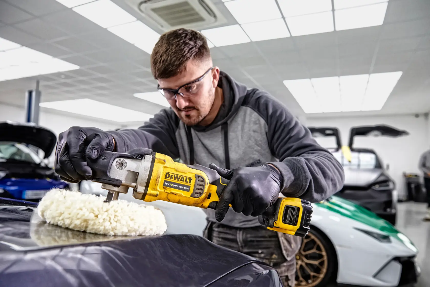 Person uses a DEWALT DCM849P2 cordless polisher to buff a car's hood in a garage.