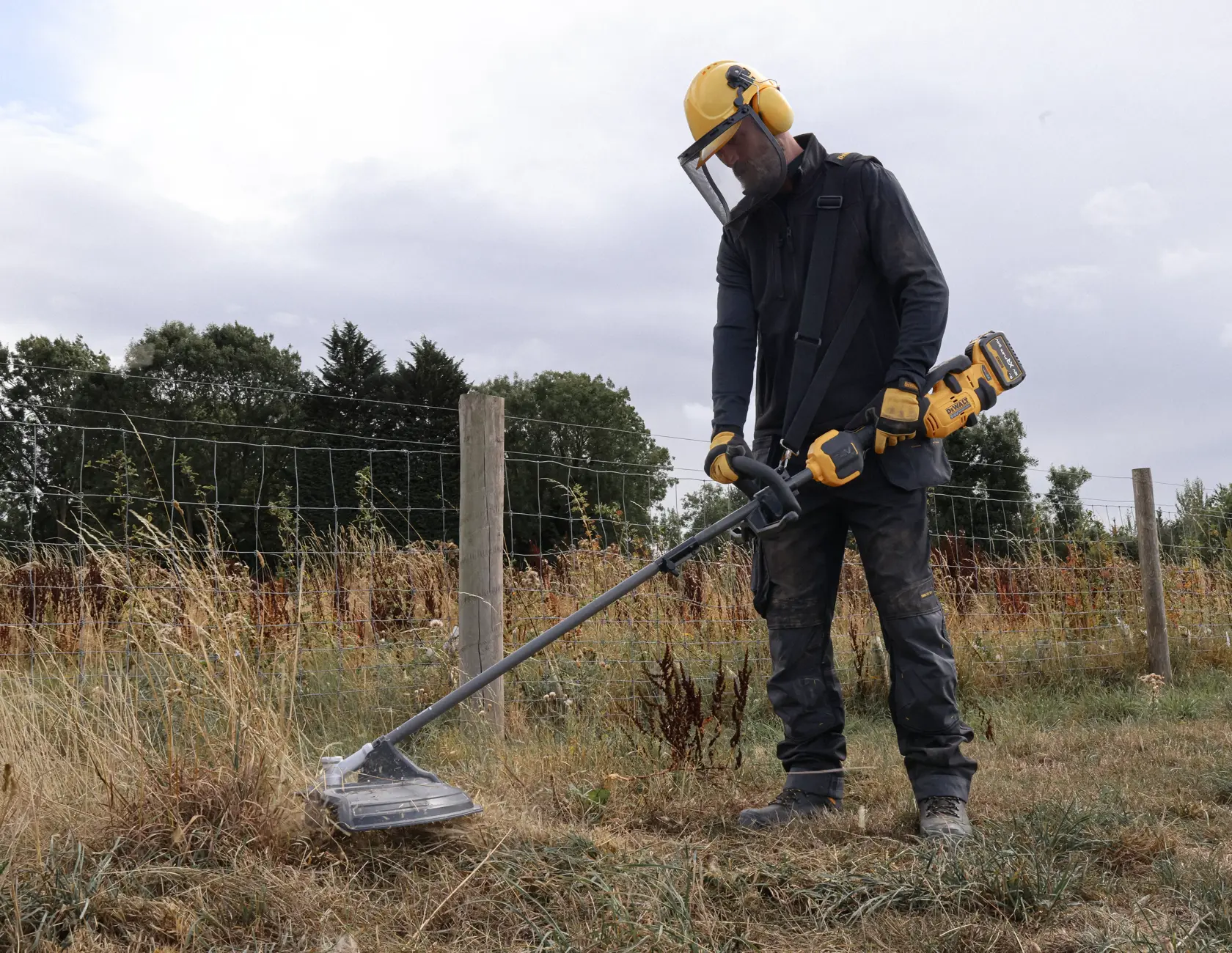 Person uses DEWALT tool outdoors; SKUs DCMASST1N, DCZ65713X1-XE, DCMASST1N-XJ. Protective gear worn.