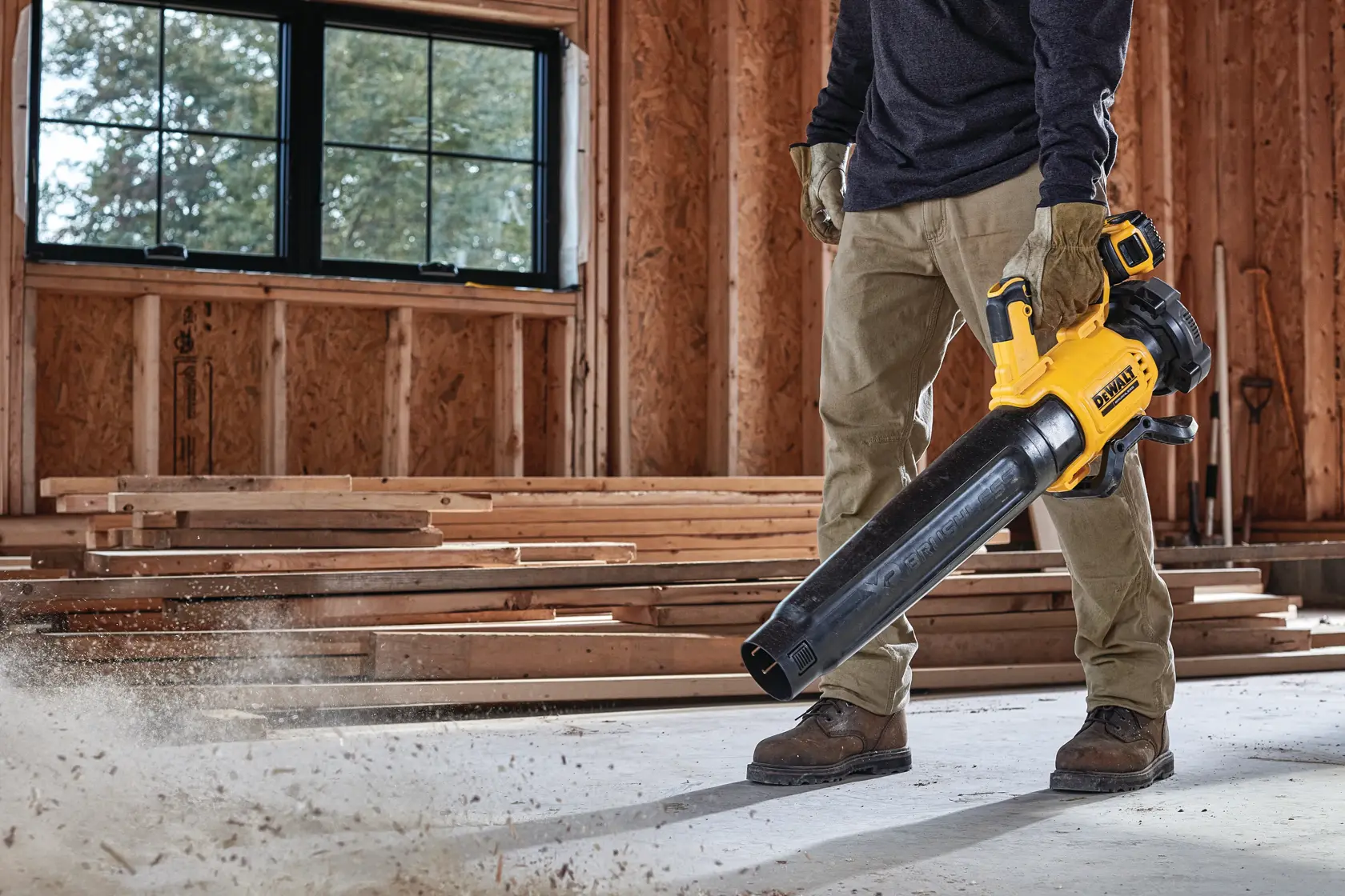 Person cleaning a construction site floor with a yellow DEWALT cordless blower.