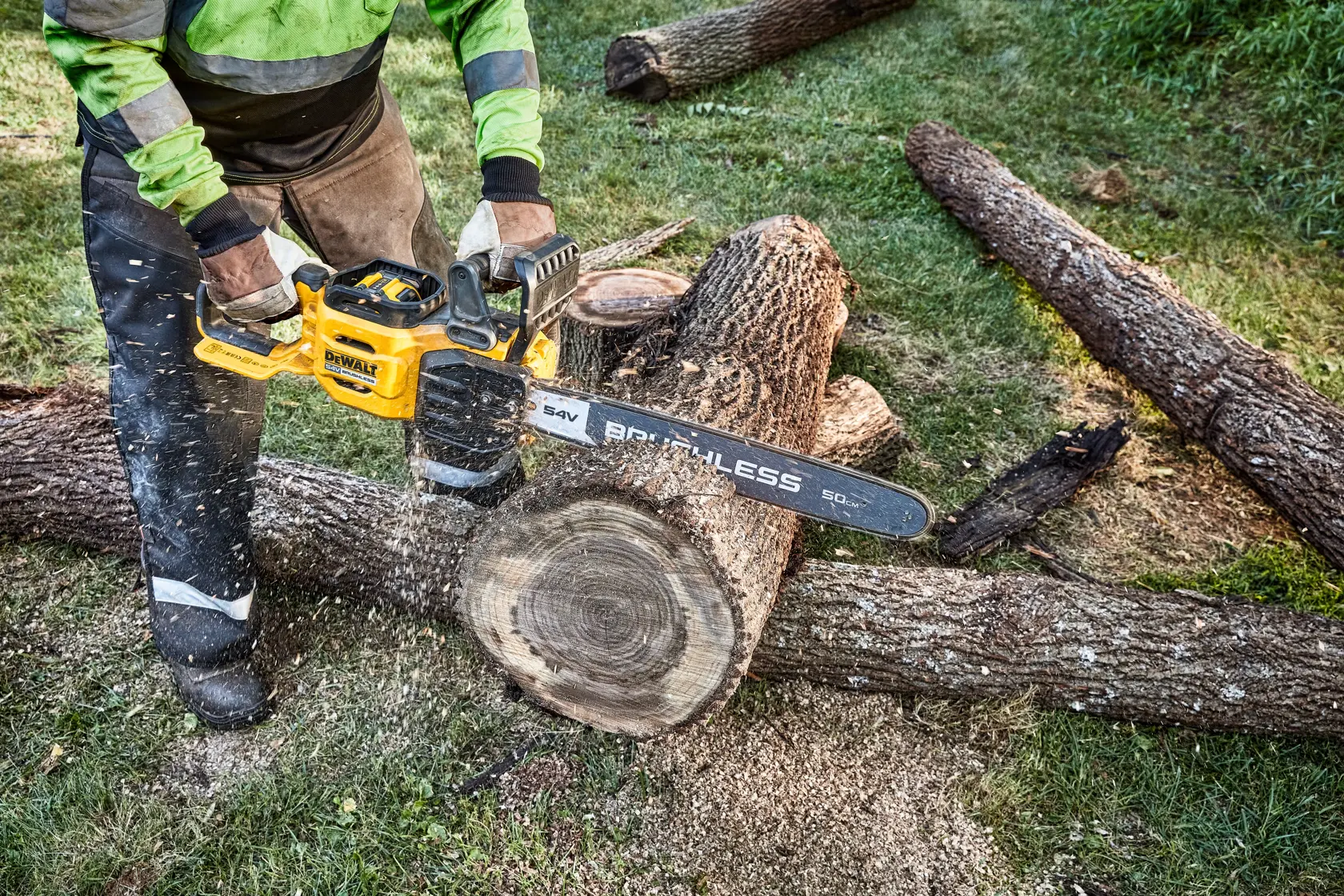 Una persona utilizza una motosega a batteria DEWALT gialla per tagliare un grosso tronco all'aperto. La motosega sta segando il legno, producendo trucioli.