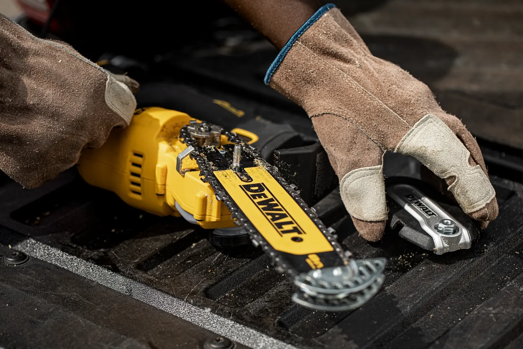 Manos con guantes ajustan una motosierra DEWALT sobre superficie negra, centrado en la hoja y herramienta.