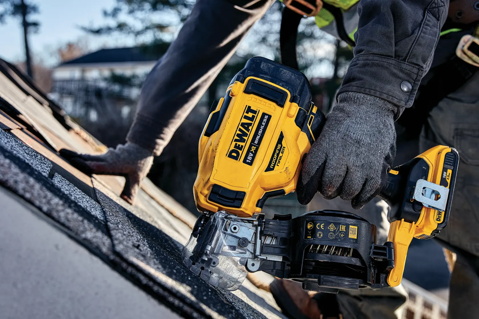 Worker using DEWALT cordless nailer on a roof, close-up of tool in action during roofing installation.