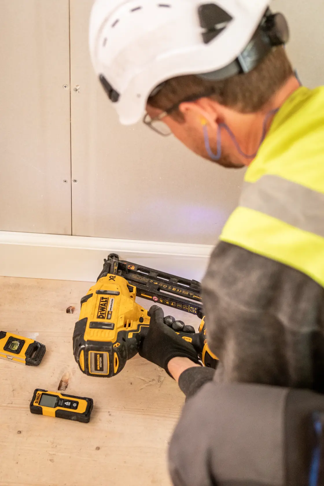 Person using a DEWALT DCN660N nailer on wood flooring, with tools nearby, wearing safety gear.