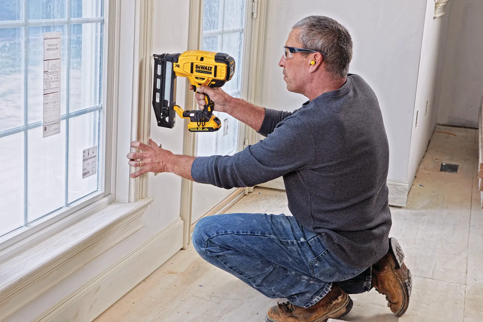Person uses a DEWALT DCN662D2 nailer on window trim in a room under construction.