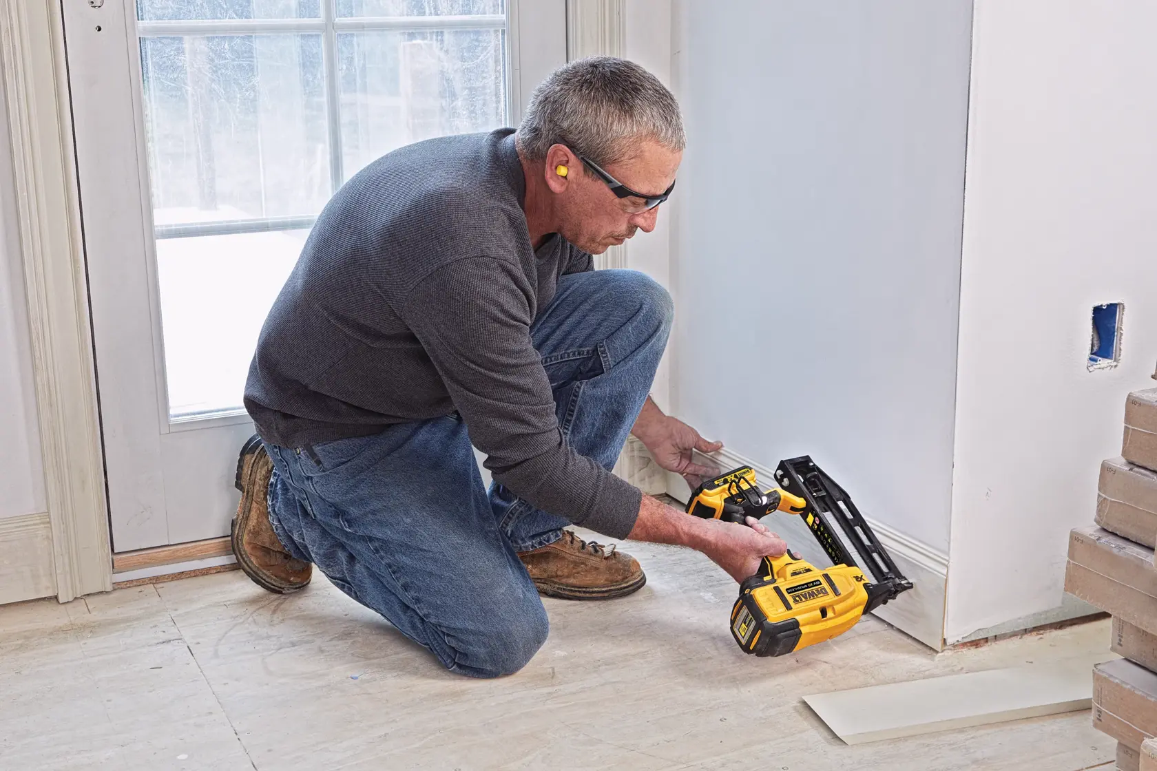 Persona usando clavadora DEWALT para fijar zócalo cerca de puerta en habitación en renovación.