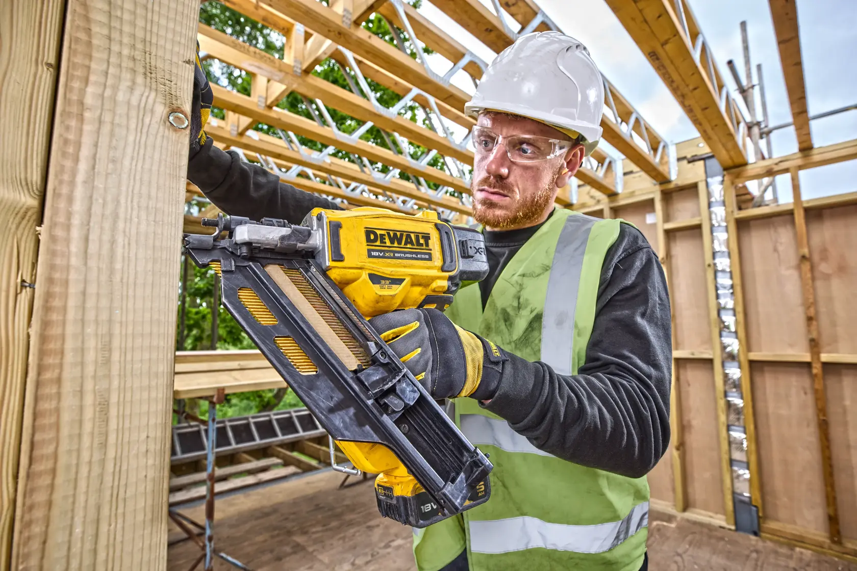 Worker uses DEWALT DCN950N nail gun on wooden beam at construction site, wearing safety gear.