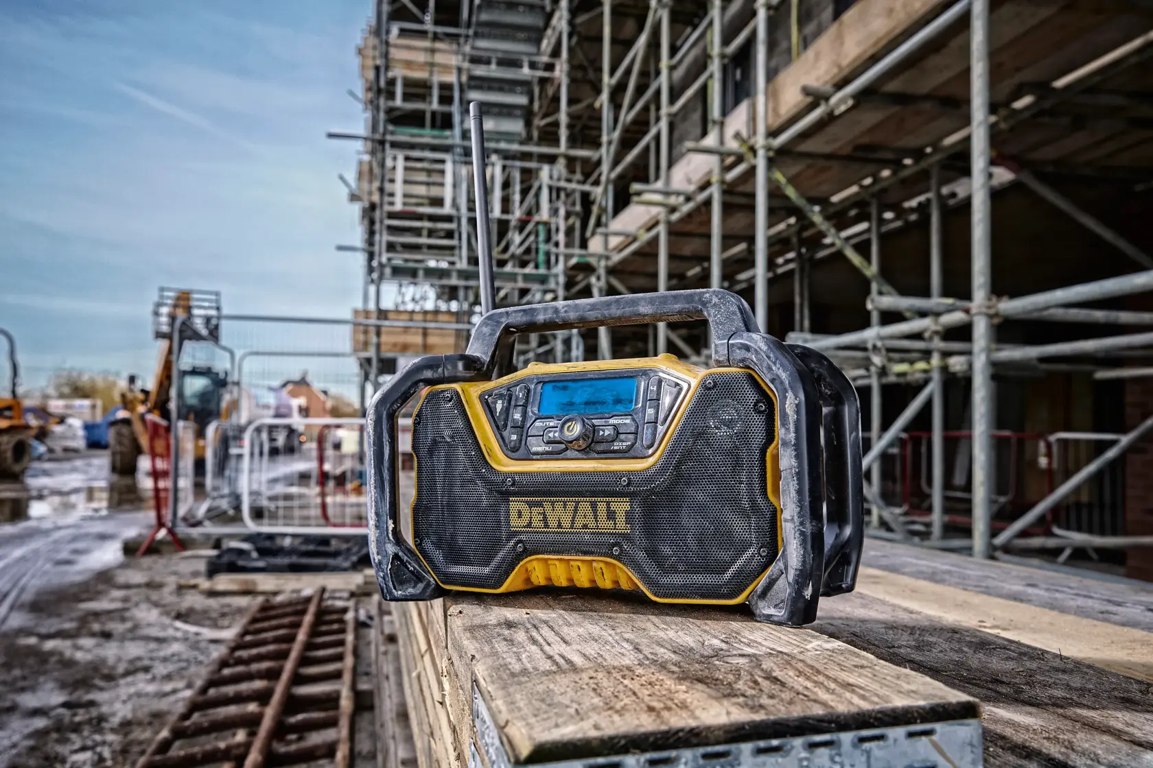 DEWALT portable radio sits on wooden planks at a construction site, surrounded by scaffolding and equipment.