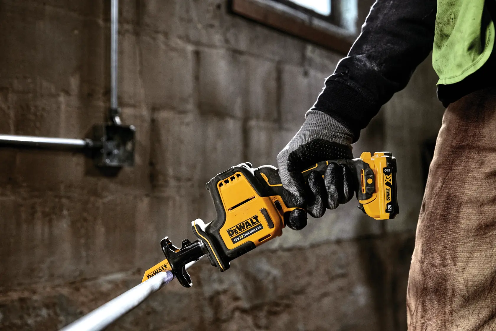 Person using a DEWALT DCS312N cordless reciprocating saw to cut a pipe in a workshop.