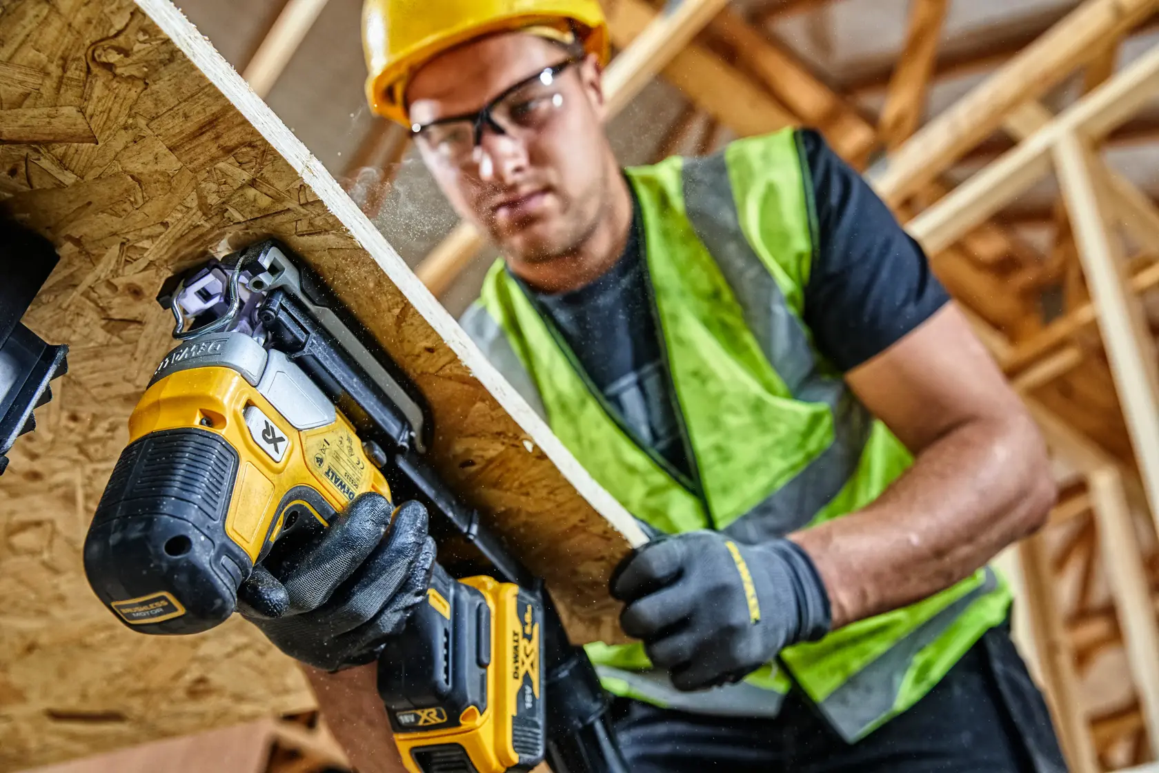 Worker uses DEWALT DCS335N jigsaw on wood panel at construction site, wearing safety vest and gloves.