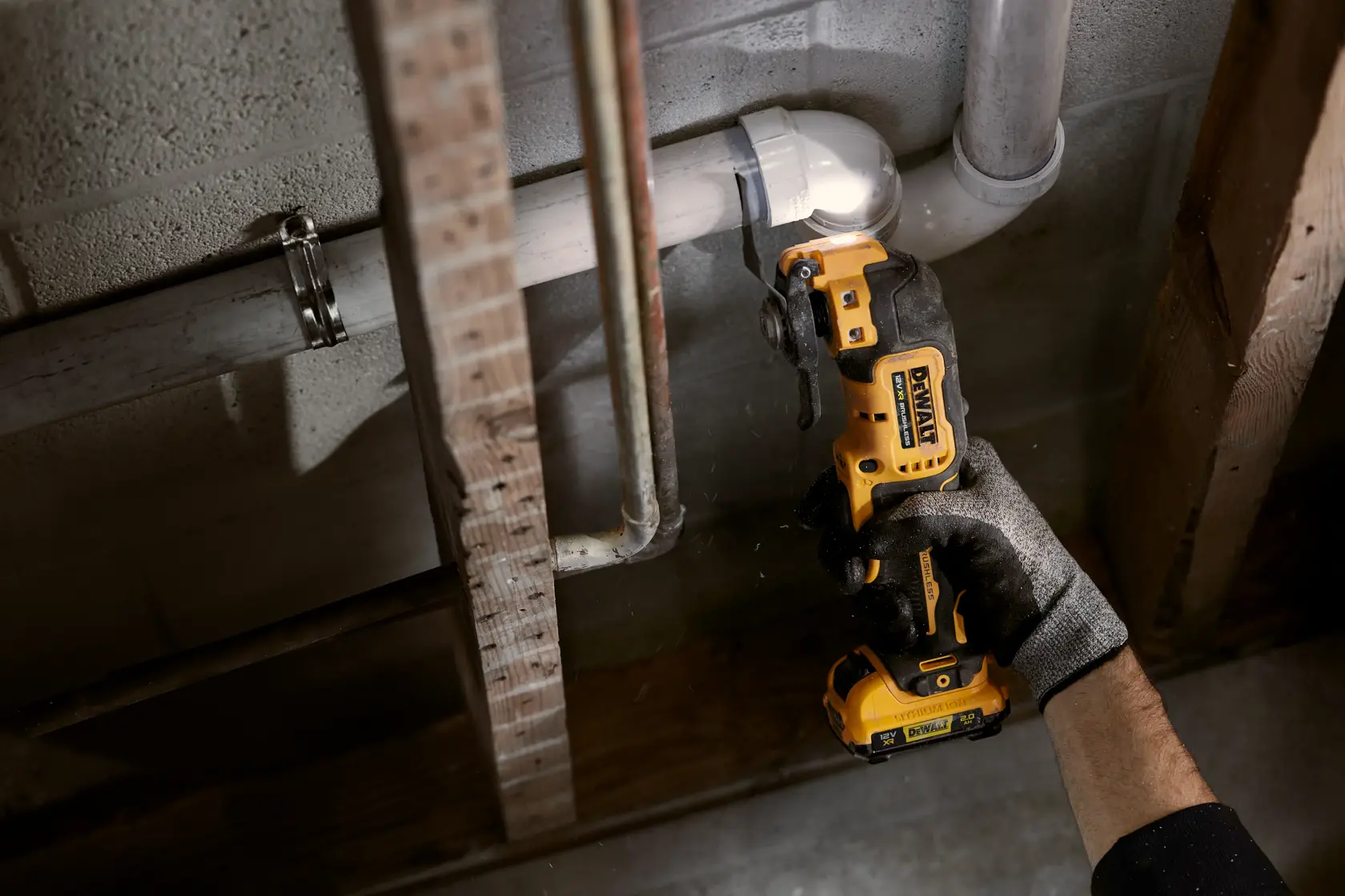 A DEWALT cordless tool is used to cut a pipe in a construction setting by a gloved hand.
