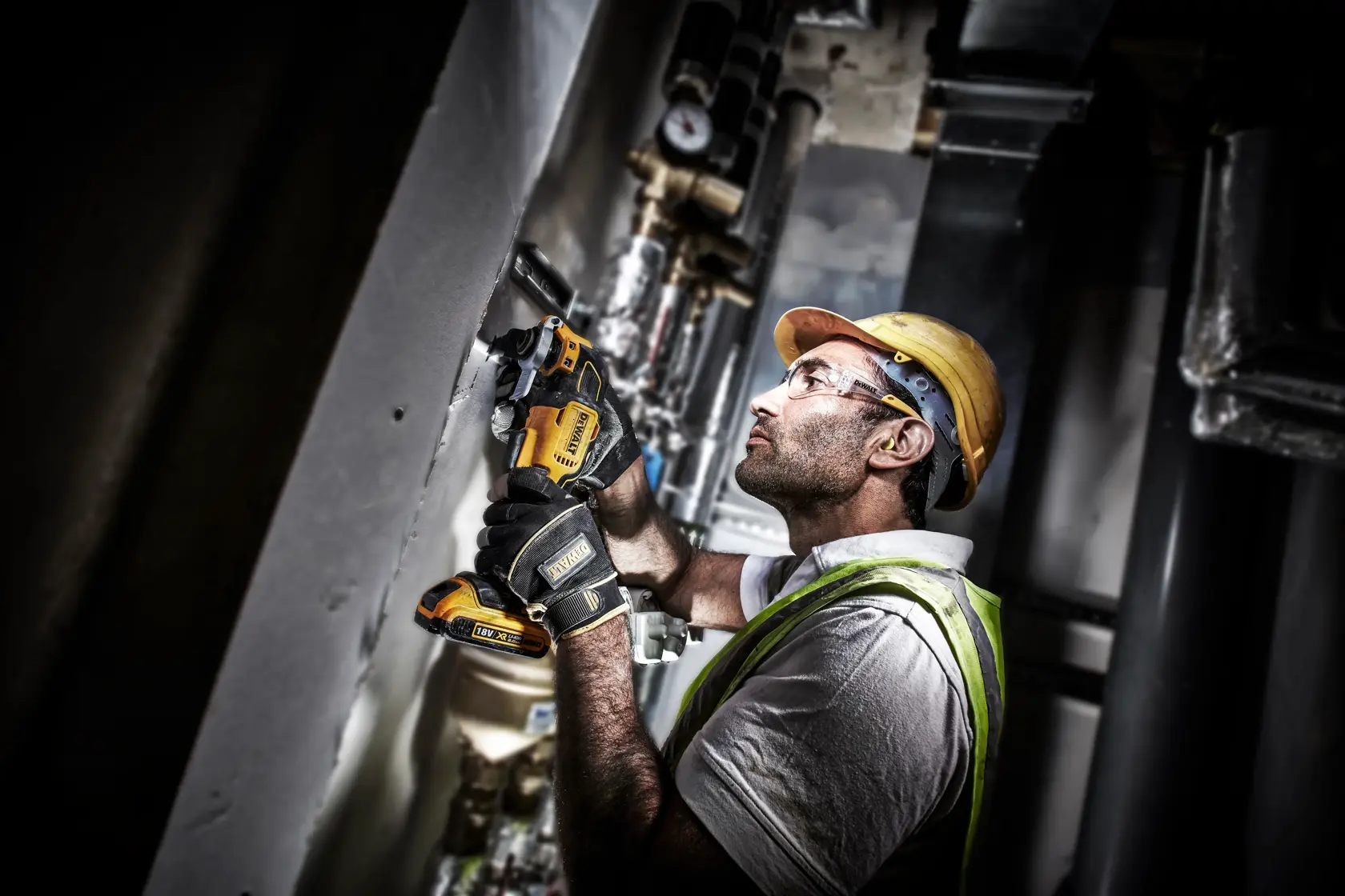 Worker uses DEWALT DCS356NT cordless tool on wall in industrial setting, wearing safety gear and gloves.