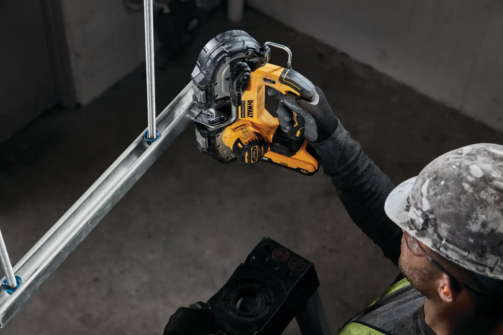 Ouvrier utilise une scie à ruban sans fil DEWALT jaune pour couper un tuyau en métal.