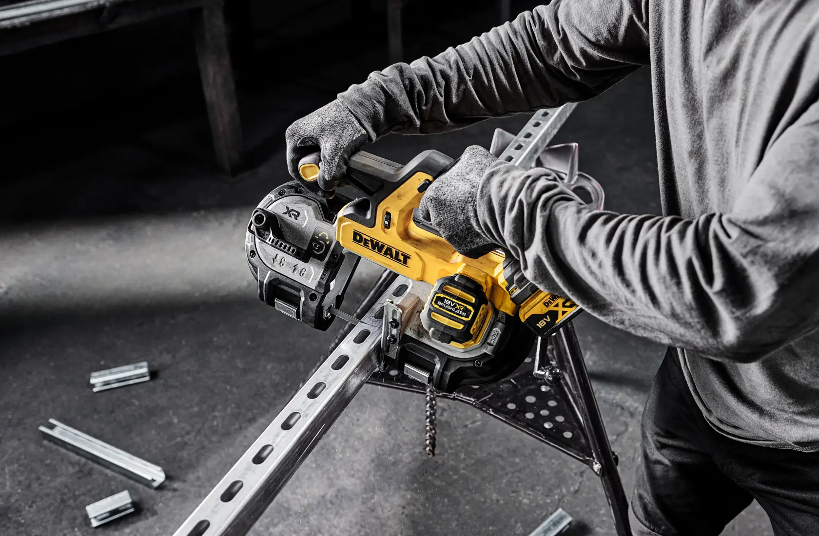 Person uses DEWALT cordless band saw to cut metal beam indoors. Saw and safety gloves are visible.