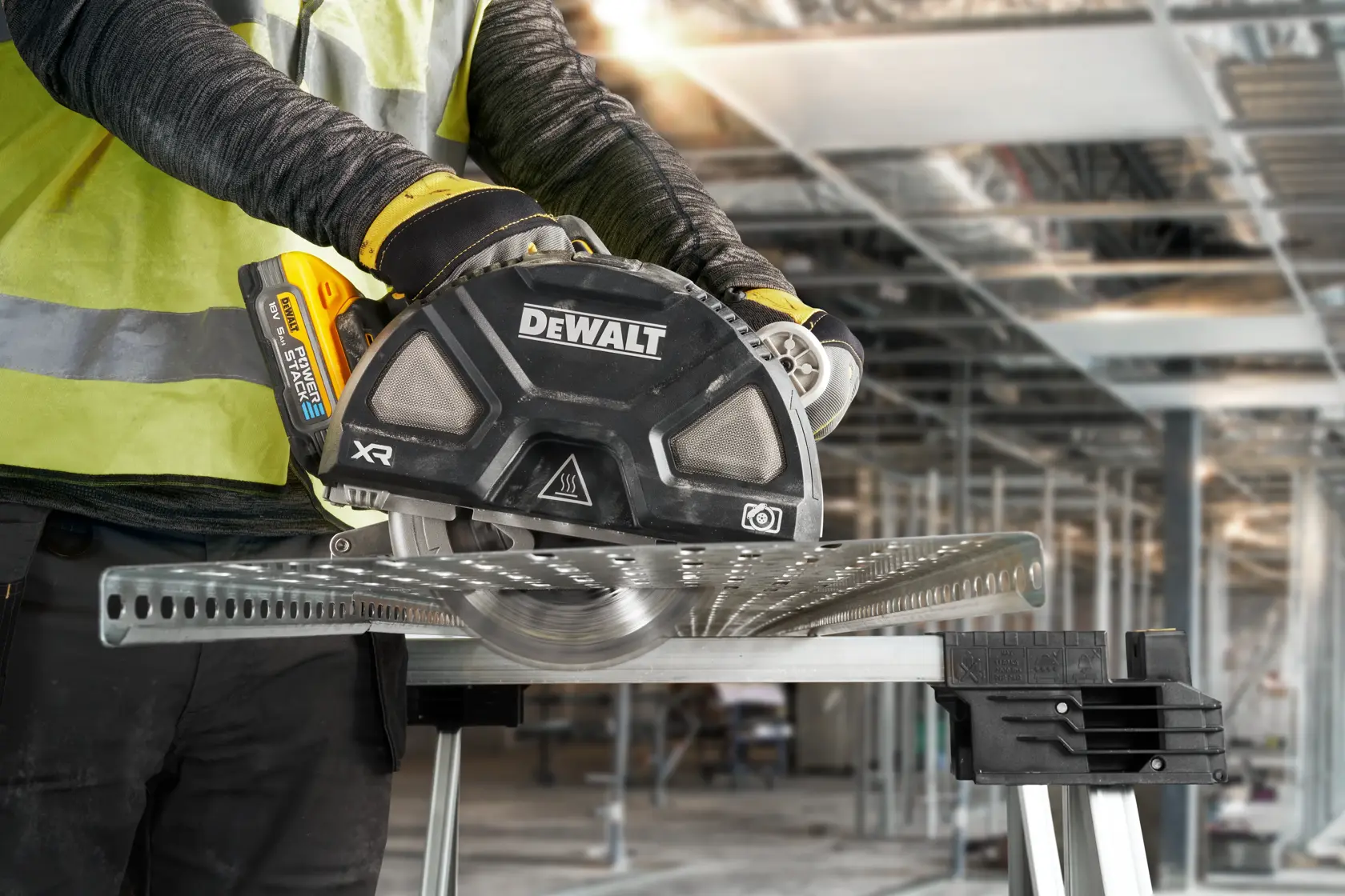 Person uses a DEWALT cordless saw to cut metal on a workbench at a construction site.