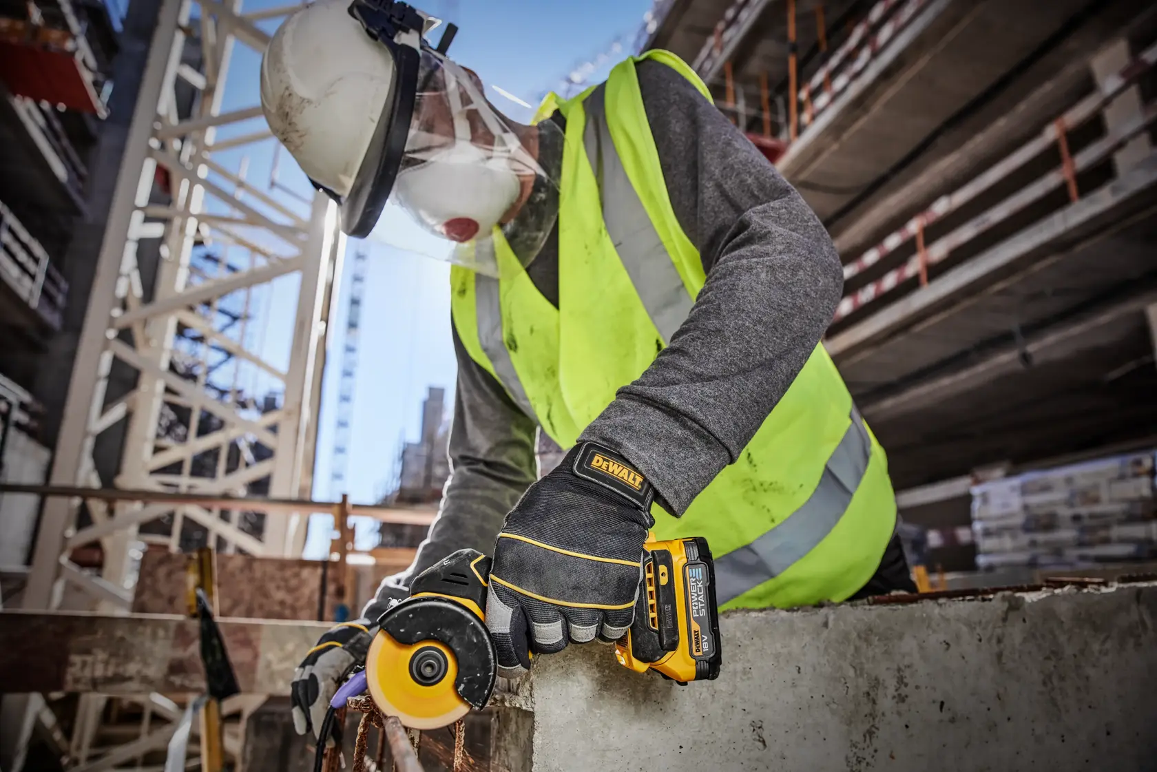 A person wearing safety gear, including a helmet, face shield, mask, gloves, and a high-visibility vest, is using a DEWALT cordless metal cutting tool, generating sparks while working on a metal surface in an industrial environment.