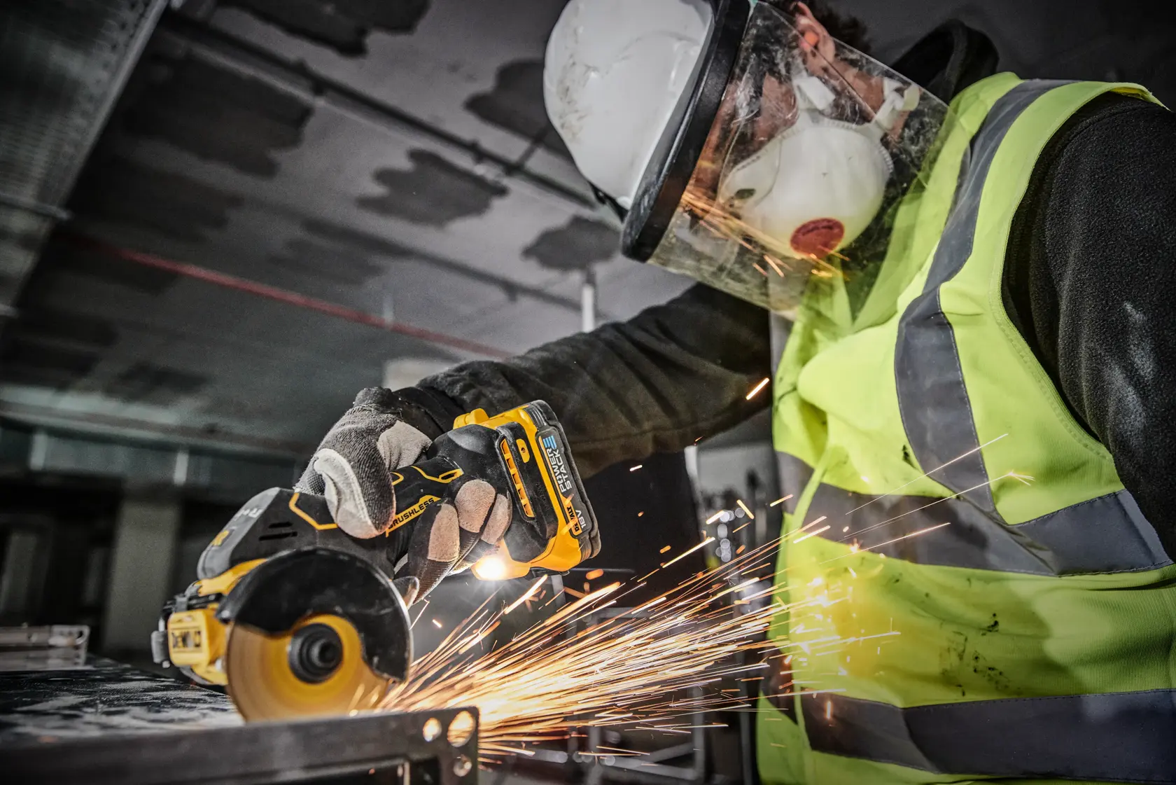 En person med sikkerhetsutstyr, inkludert hjelm, ansiktskjerm, maske, hansker og refleksvest, bruker et DEWALT DCS438N batteridrevet verktøy for å kutte metall, mens det oppstår gnister.