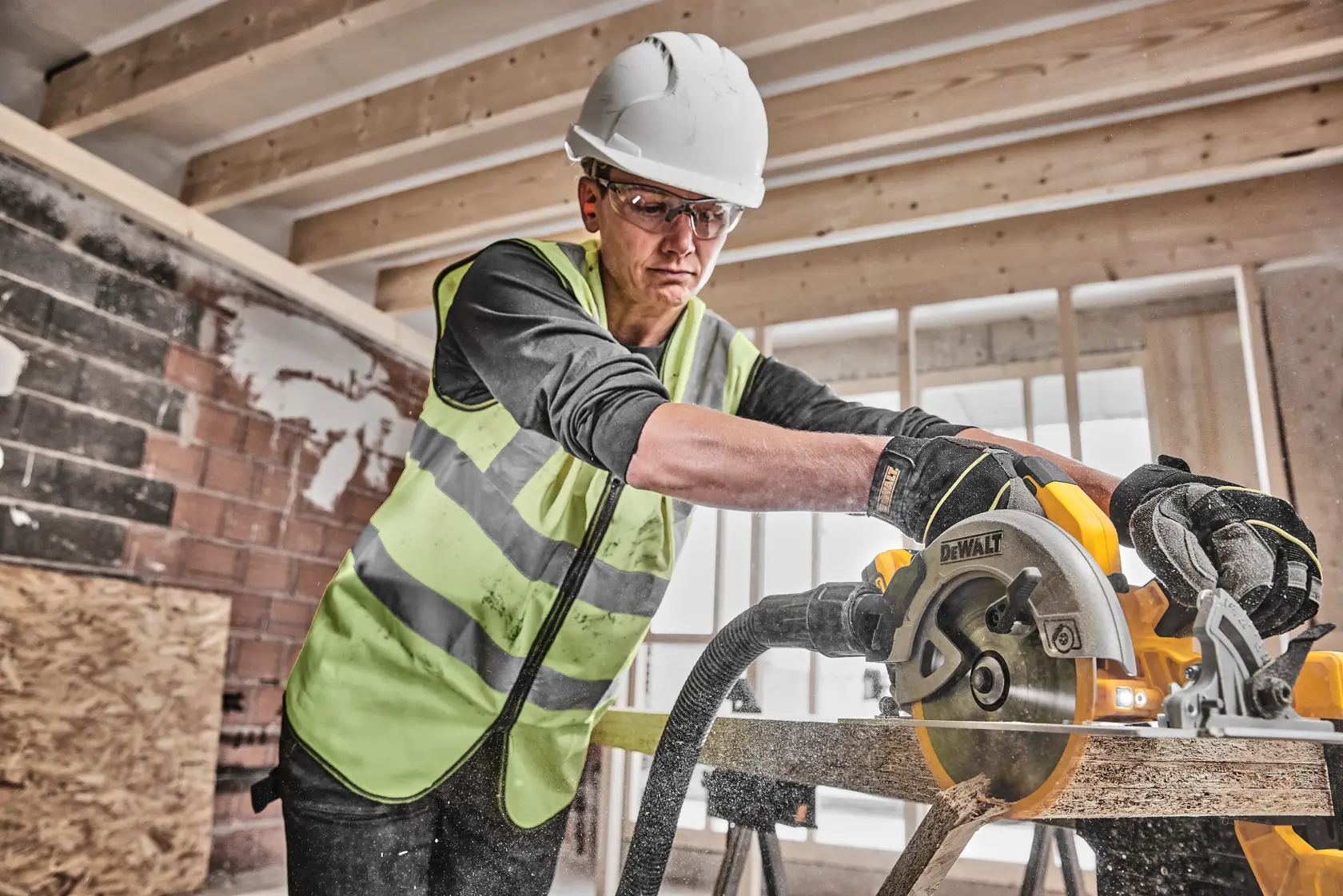 Worker uses DEWALT circular saw to cut wood at construction site, wearing safety gear and gloves.
