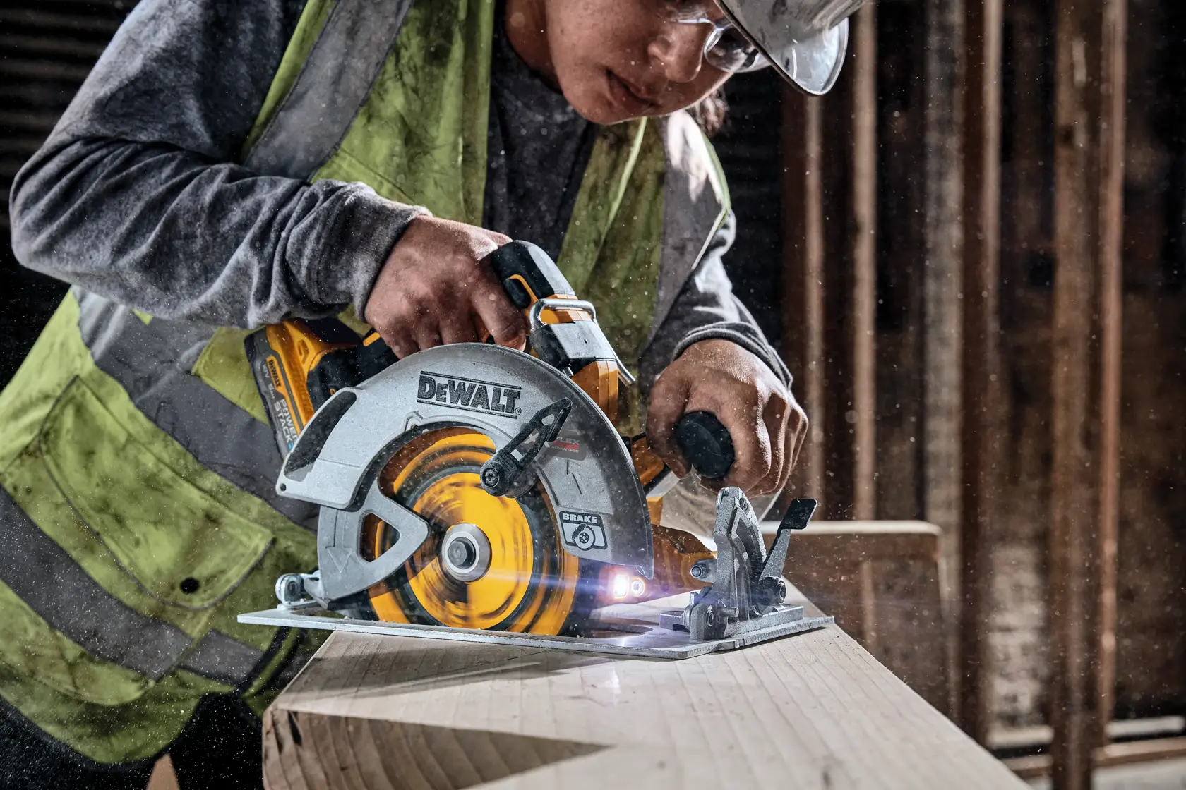 Eine Person mit Sicherheitsausrüstung verwendet eine kabellose DEWALT Kreissäge, um einen Holzbalken in einer Werkstatt oder auf einer Baustelle zu schneiden.