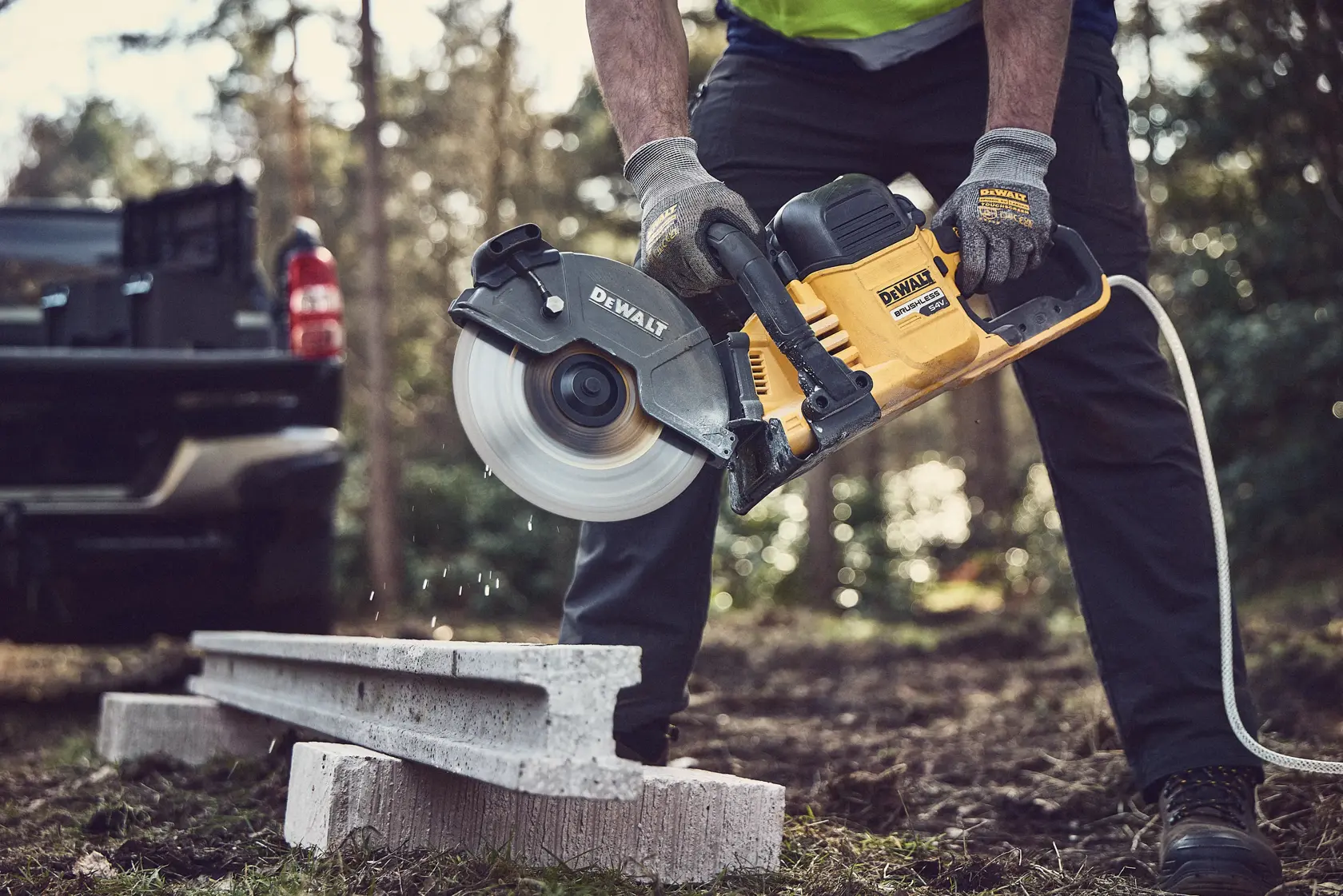 Person using a DEWALT DCS691X2 saw to cut concrete outdoors, wearing gloves for safety.