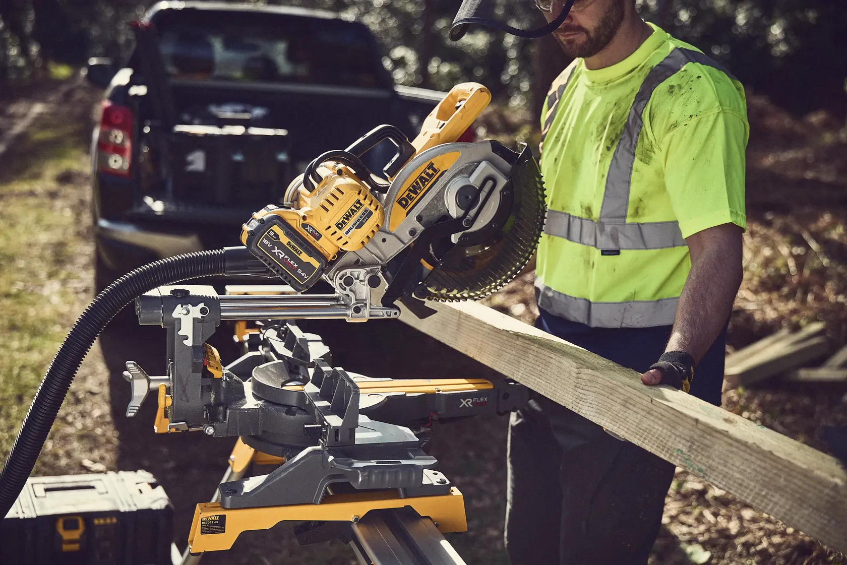 DEWALT DCS727N Säge im Einsatz, schneidet Holz. Arbeiter mit Sicherheitsweste im Freien neben Fahrzeug.