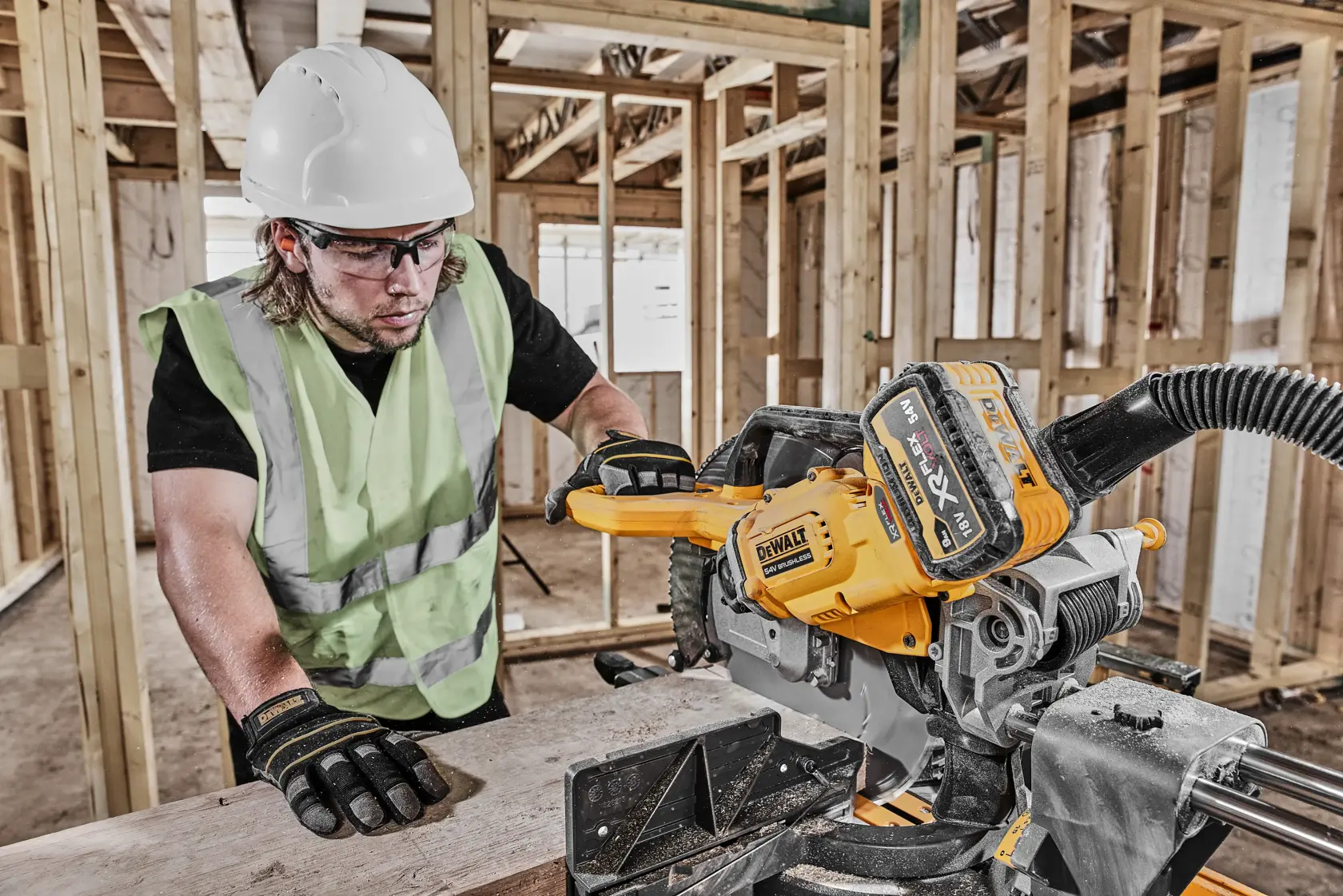 Arbeiter nutzt DEWALT DCS781N Säge auf Holzbrett, Baustelle, mit Schutzkleidung.